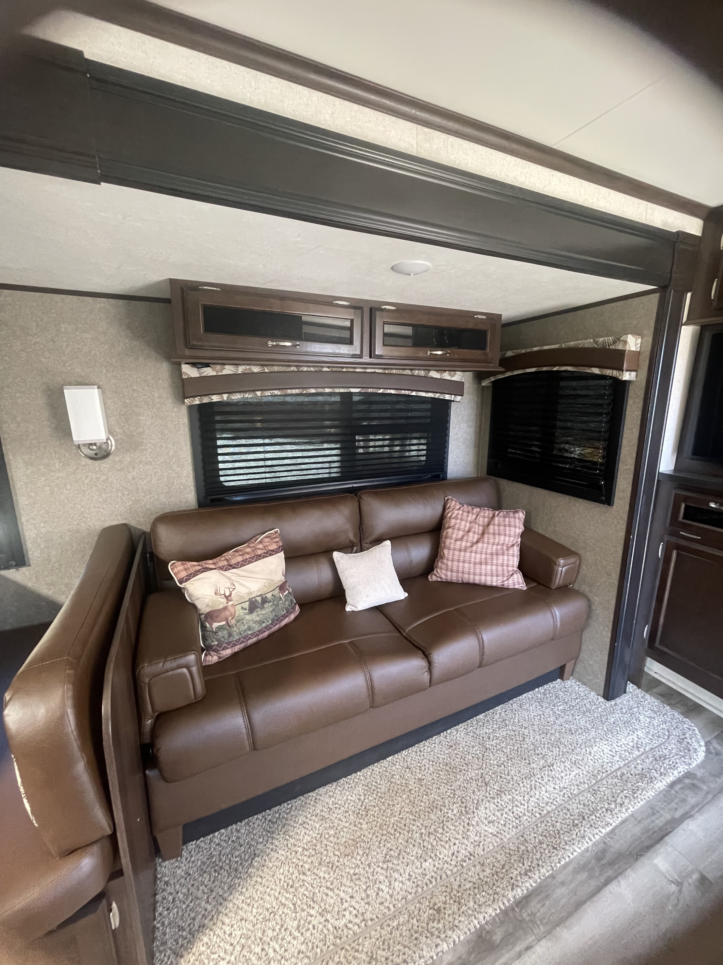 Cozy RV rental living space: brown sofa, windows, overhead cabinets, and soft rug for comfort.. Jayco Jay Flight 2018