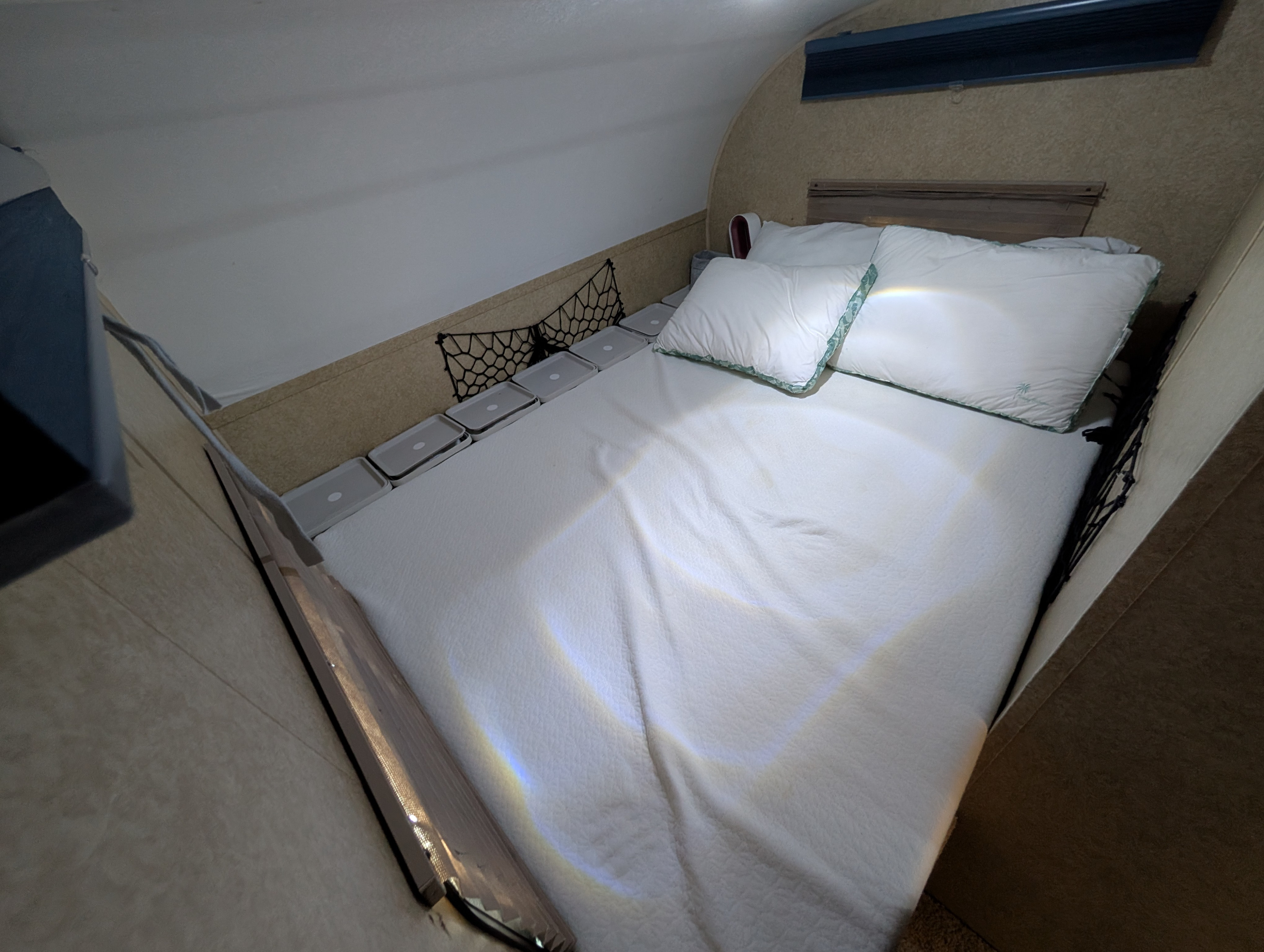 RV rental bedroom features a comfy white bed, pillows, and bedside storage with bins & a net. Refracted light adds color.. Forest River V-Cross Vibe 2012