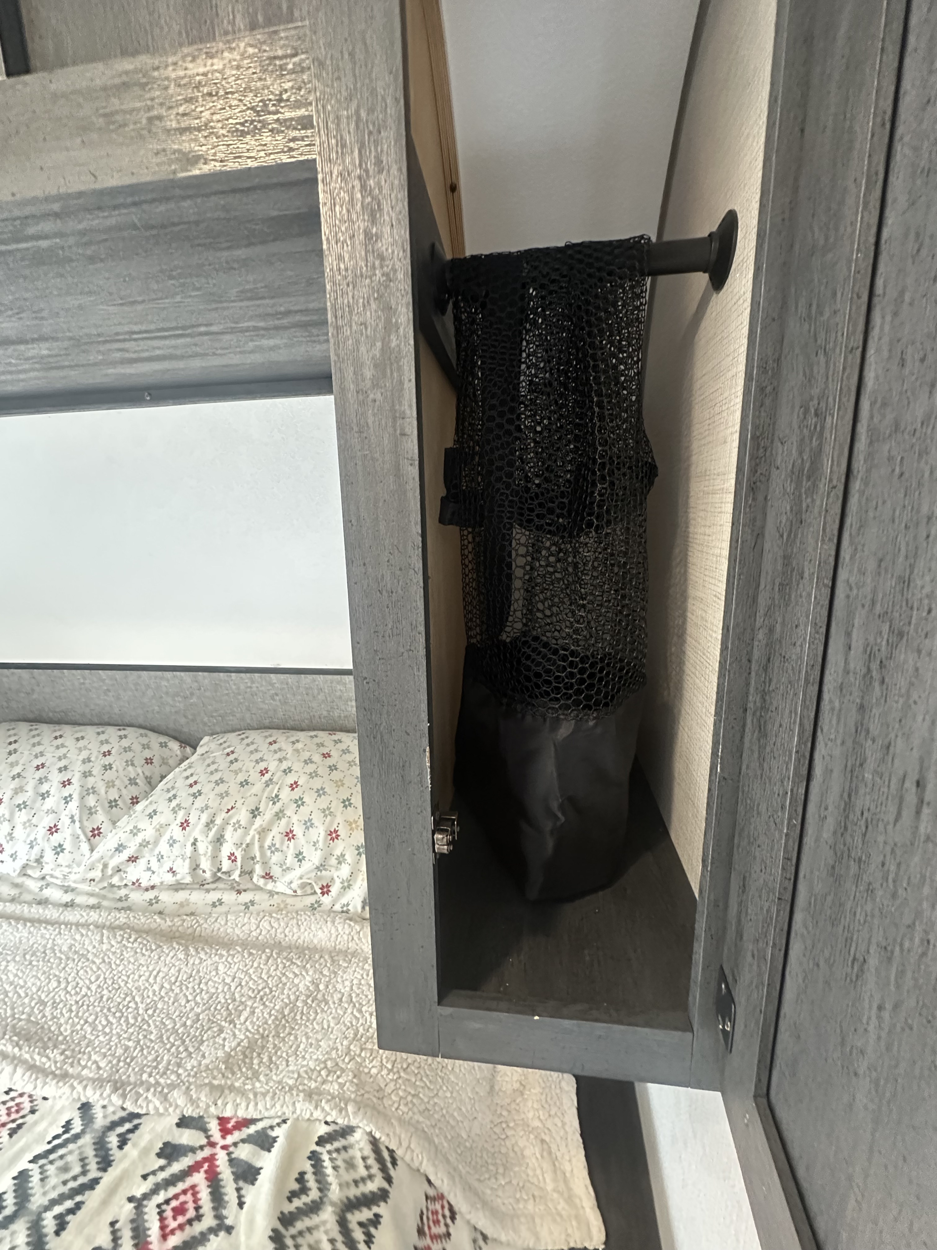 Inside an RV rental: a cozy bed with patterned pillows, and a gray overhead cabinet featuring a hanging mesh laundry bag.. Ozark Lite 2021
