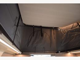 This RV rental's pop-top tent roof is raised, revealing a spacious elevated sleeping area with a light ceiling.. Ford Triton 2024