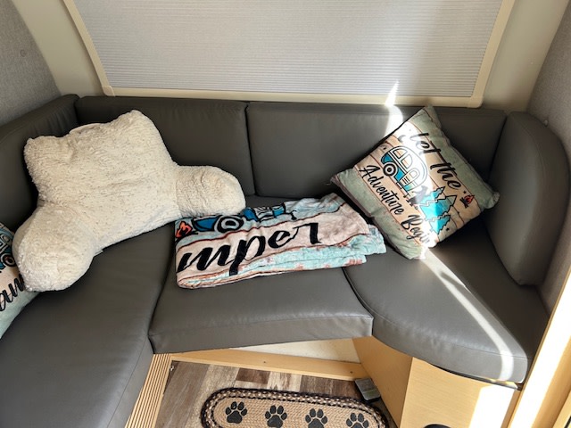 Relax in this RV rental's comfy grey seating with a fluffy backrest pillow, 'Camper' blanket, and 'Adventure Begins' pillow.. nuCamp T@B 2022