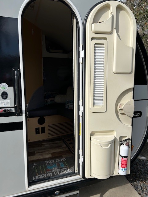Inside an RV rental: open door reveals a cozy interior, built-in storage, and fire extinguisher for traveler safety.. nuCamp T@B 2022