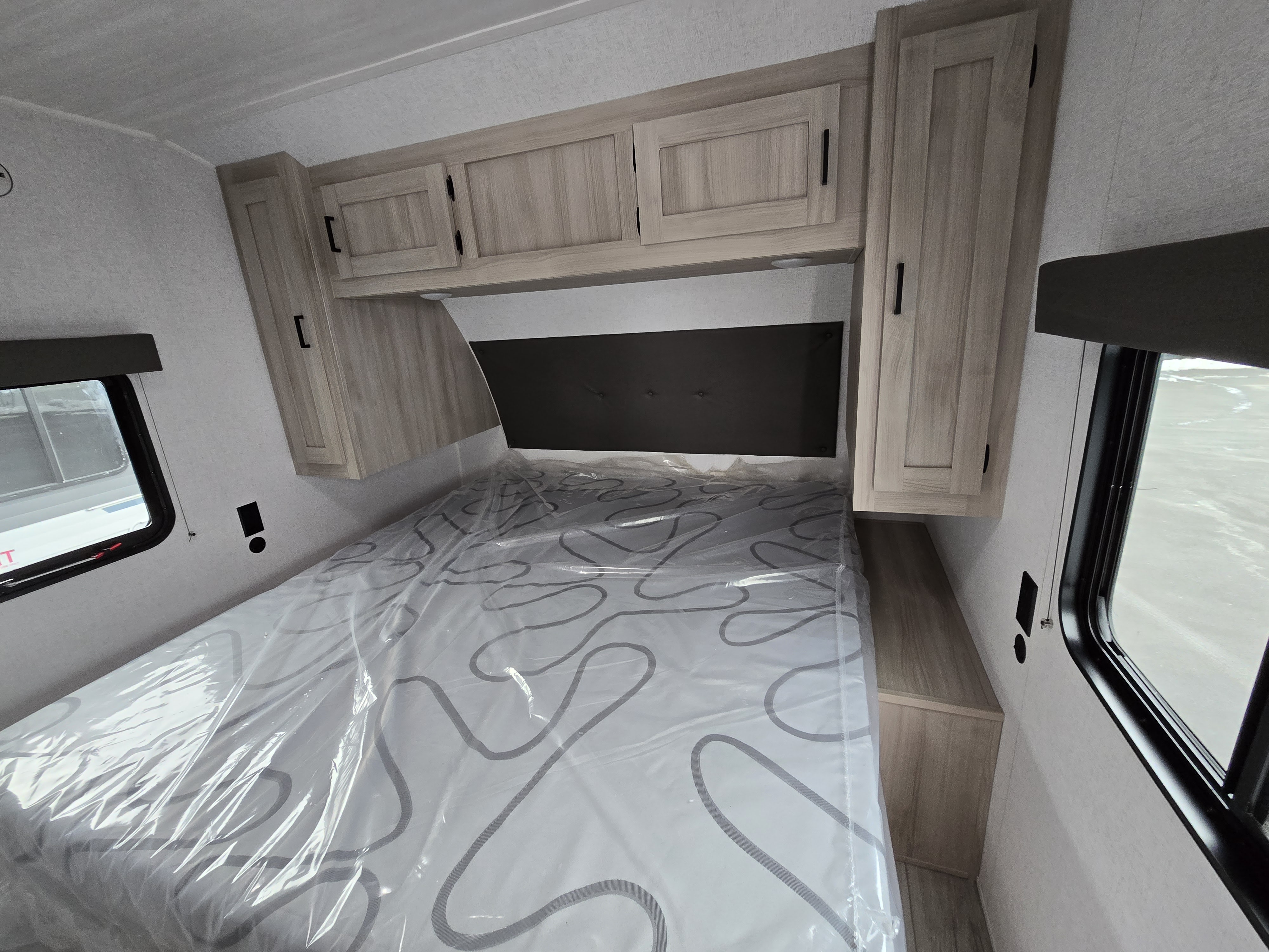 Inside an RV rental: a clean bedroom with light-toned cabinets, a window, and a bed with a plastic-covered mattress.. East to West Della Terra 241BH 2025