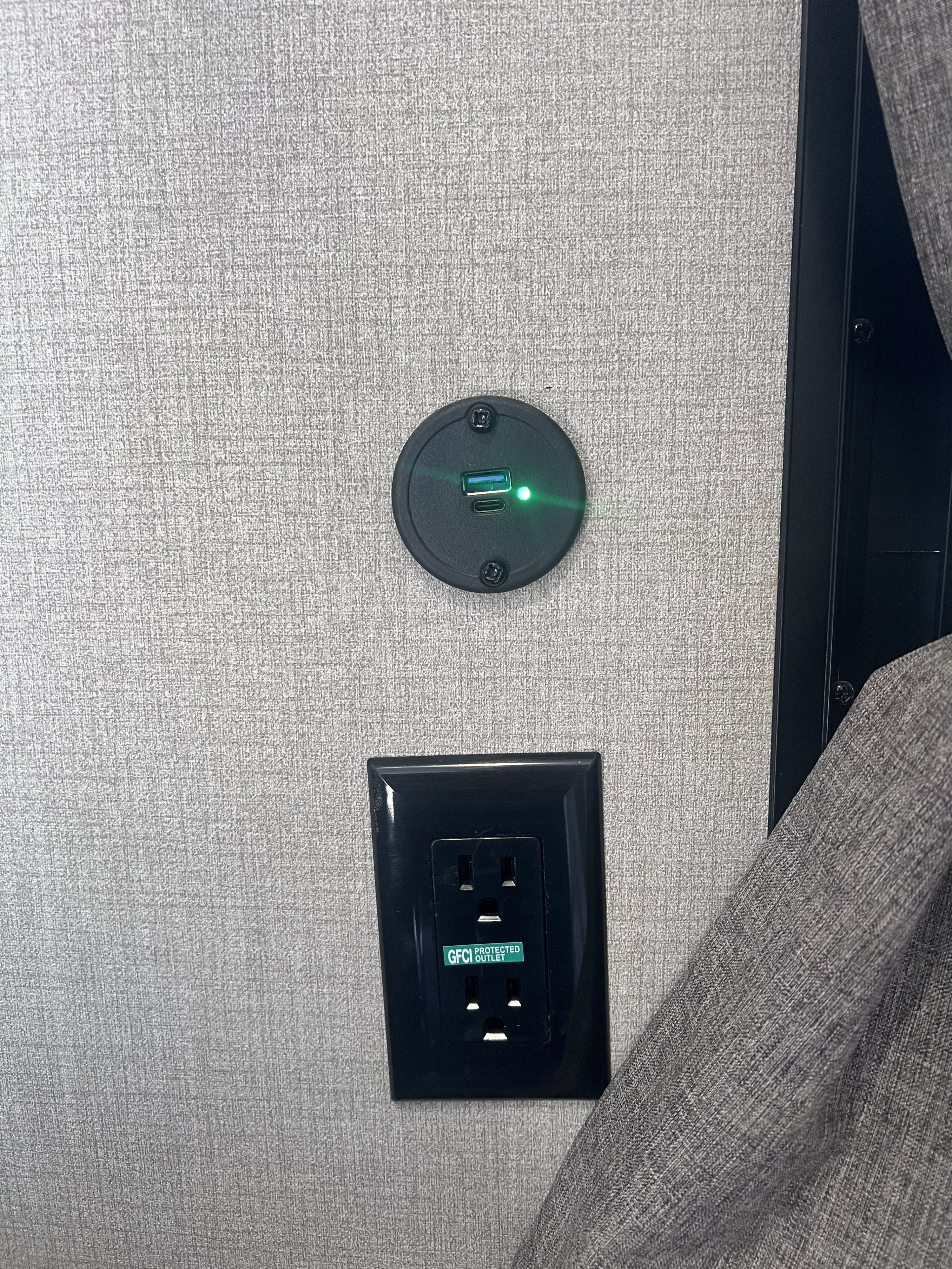 RV rental interior: A wall with a black USB charger (green light) and a GFCI protected outlet, next to a grey curtain.. Coachmen 164BHX 2023