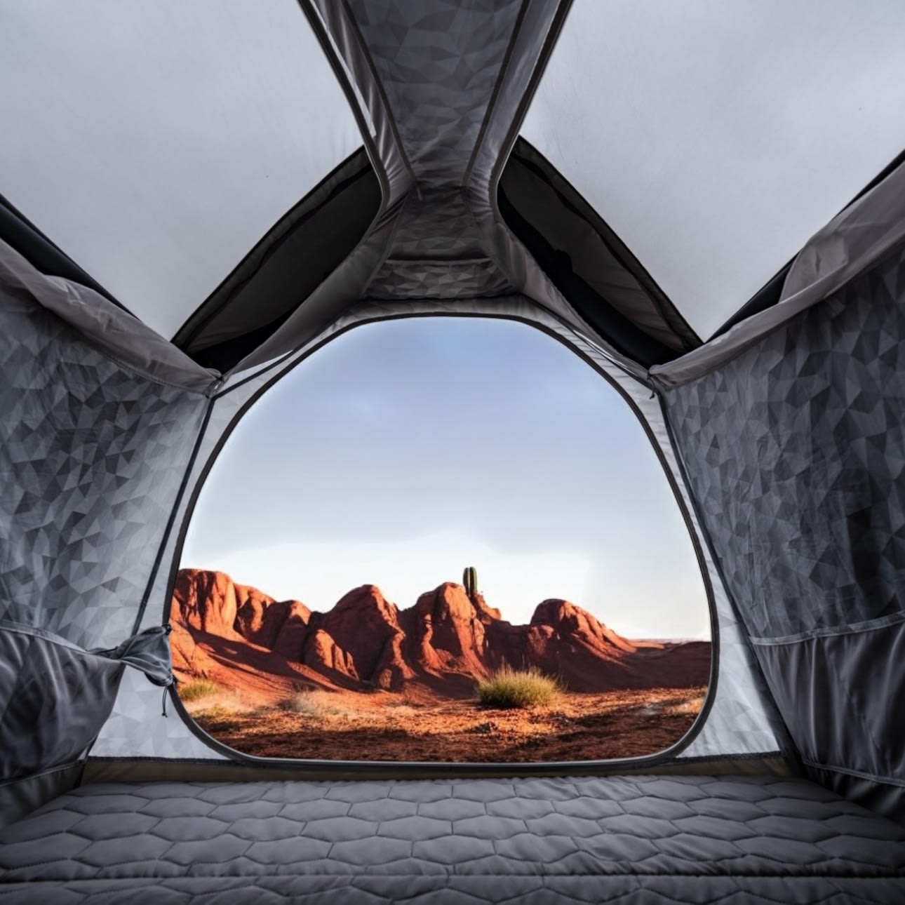 Inside a gray tent, a comfortable mattress. Outside, red desert mountains & a cactus against a blue sky. Explore with an RV rental.. Tesla Cybertruck 2024