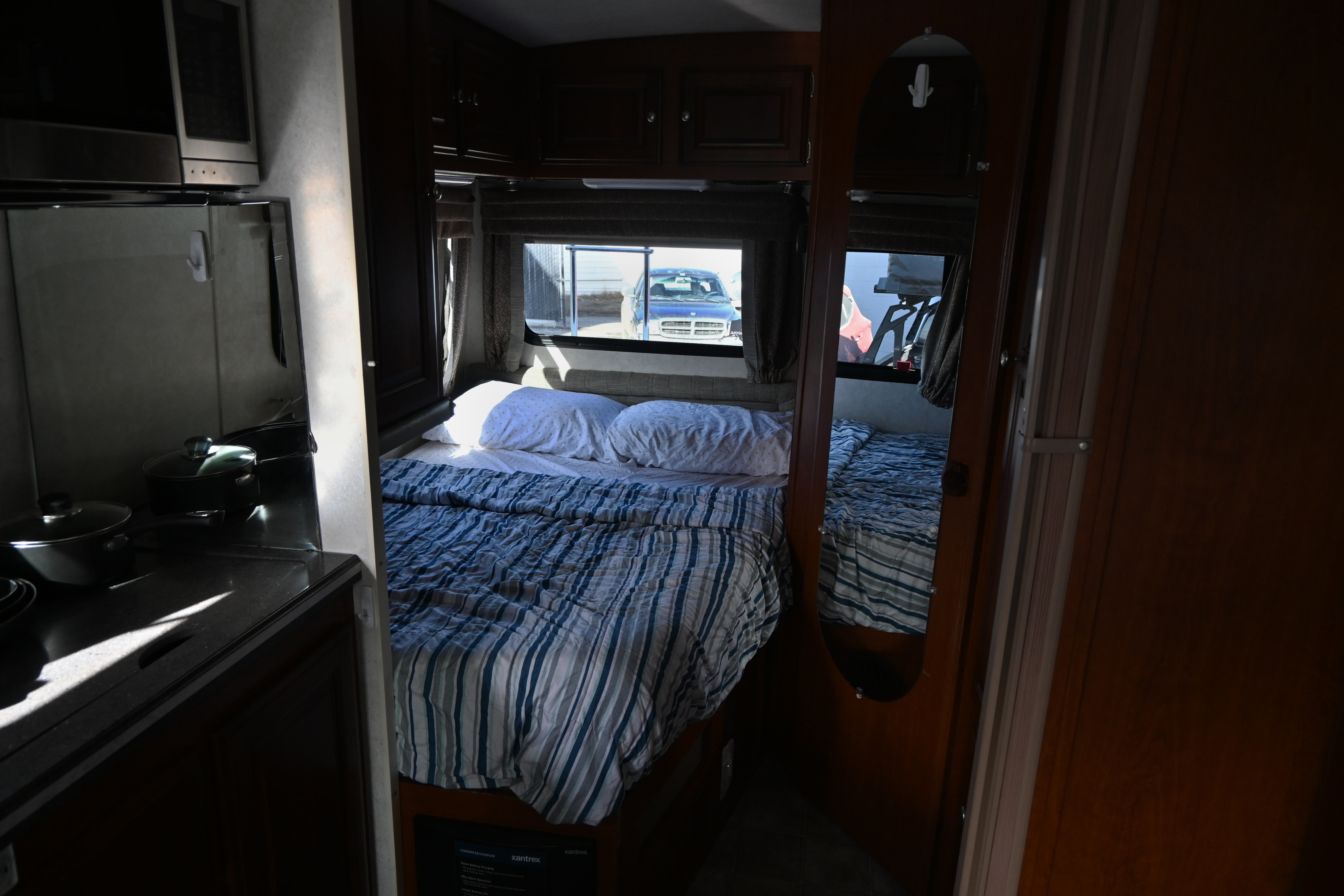 RV rental bedroom with striped comforter, kitchen counter & microwave. Sunlight illuminates the space, showing a truck outside.. Phoenix Cruiser M-2350 Sprinter Slide 2012