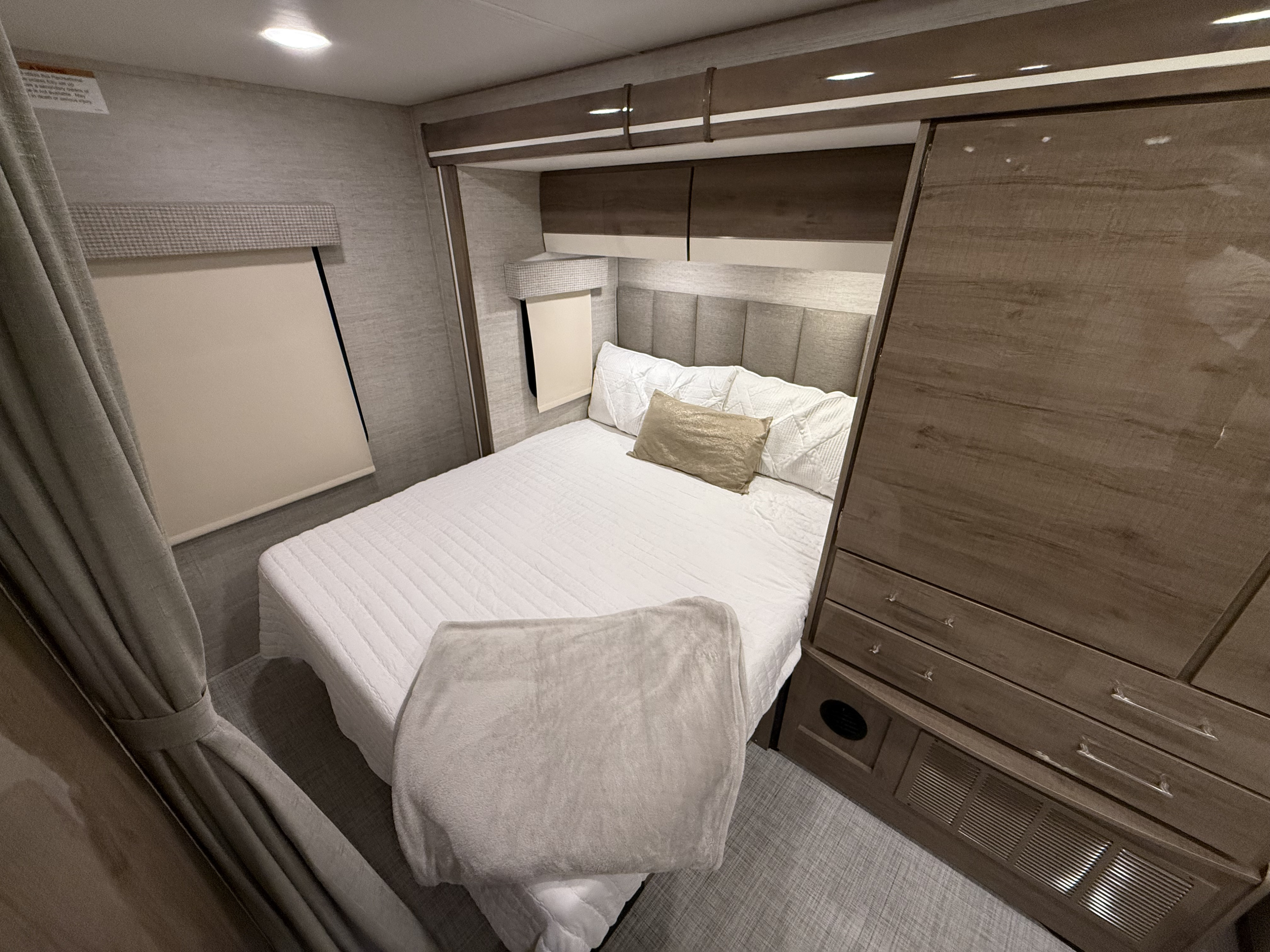 Spacious RV rental bedroom with a queen bed, overhead storage, and wardrobe. Ideal for comfortable travel accommodation, featuring neutral tones.. Entegra Coach Qwest 24L 2022