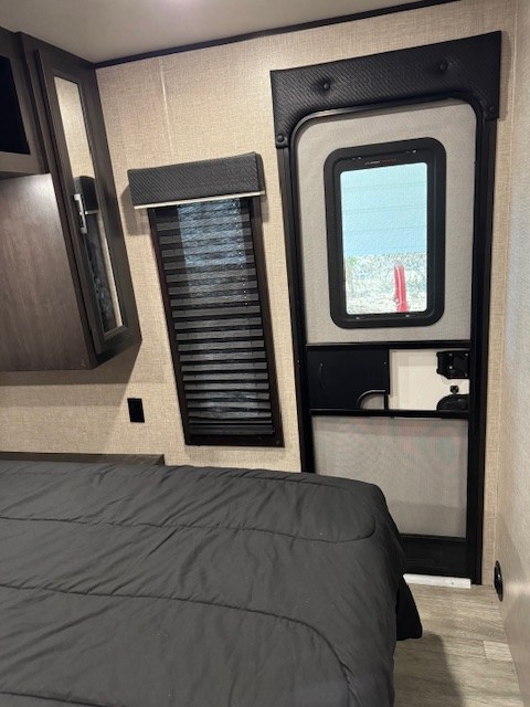 RV rental bedroom featuring a comfy bed, a window with blinds, and an exterior screen door.. Jayco Jay Flight 2023