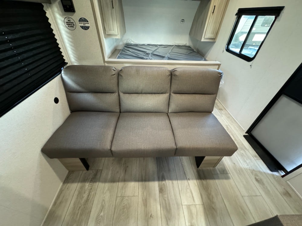 Spacious RV rental interior featuring a comfortable three-person sofa, bed area, and wood-look flooring. Ideal camper living space.. Forest River East toWest SilverLake 25bhle 2024