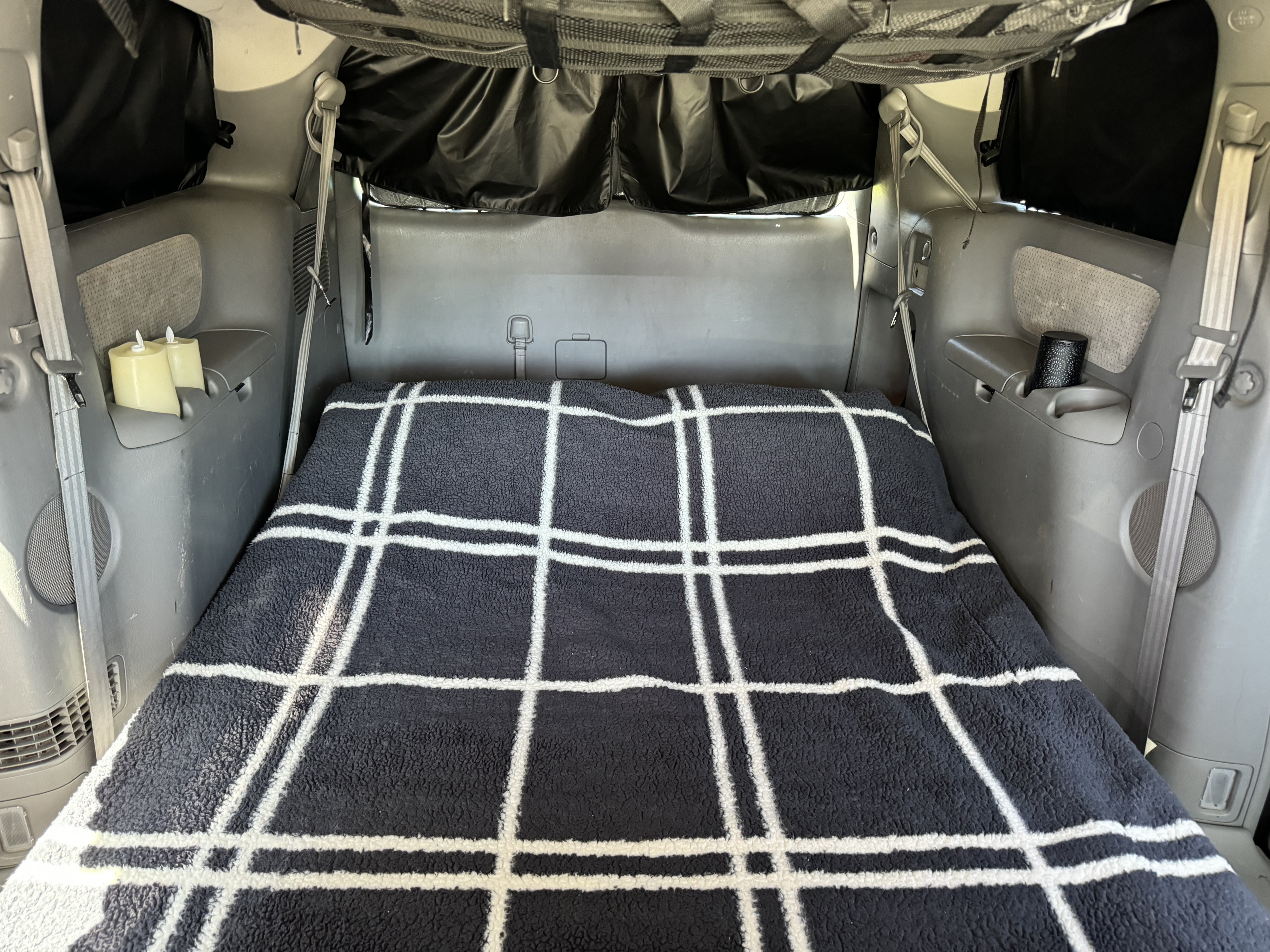 RV rental alternative: The back of a vehicle converted into a bed with a plaid blanket and privacy window covers.. Toyota Sienna 2009