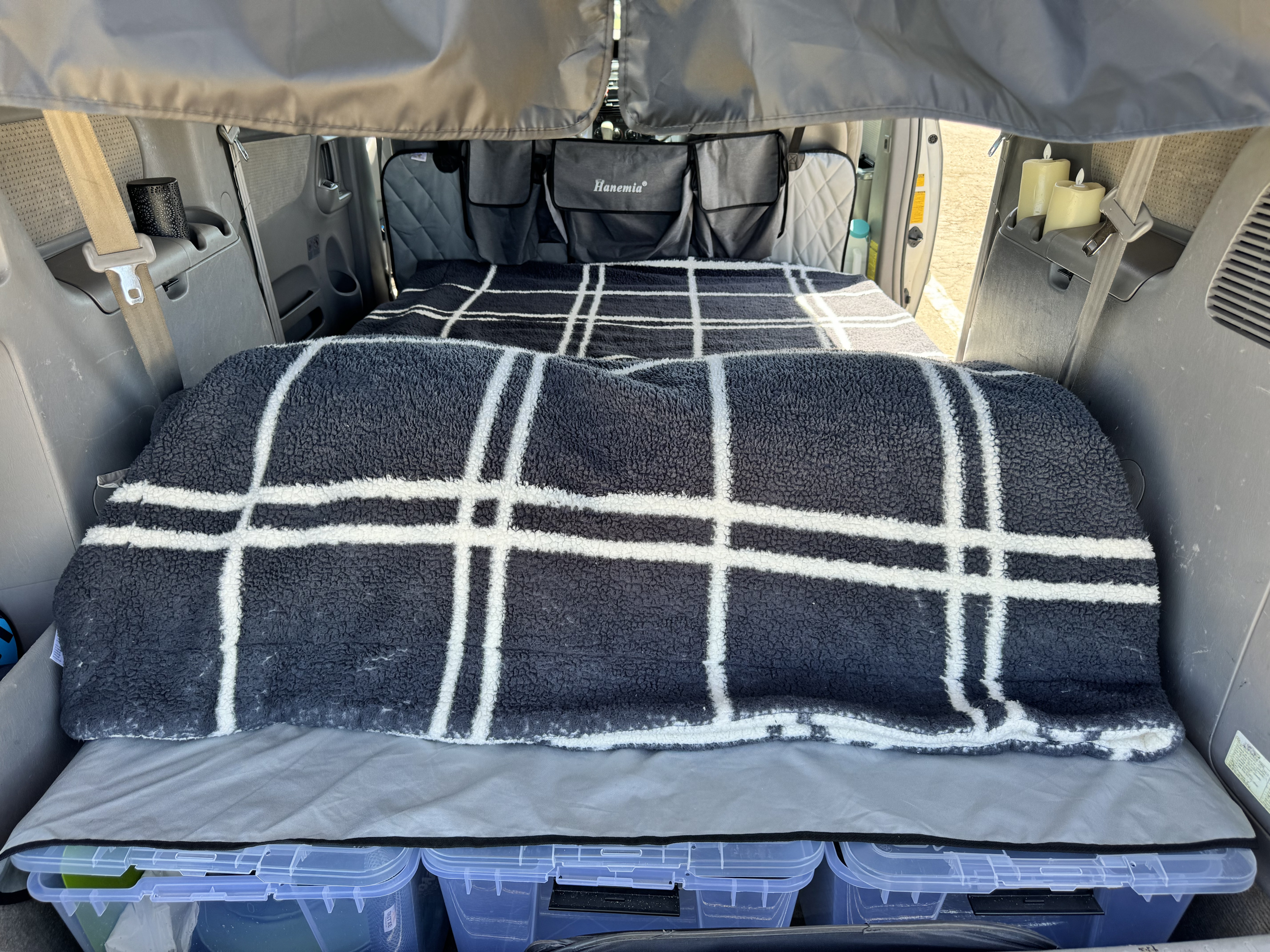 This RV rental interior features a cozy bed with a plaid blanket, storage bins, and Hanemia hanging organizers.. Toyota Sienna 2009