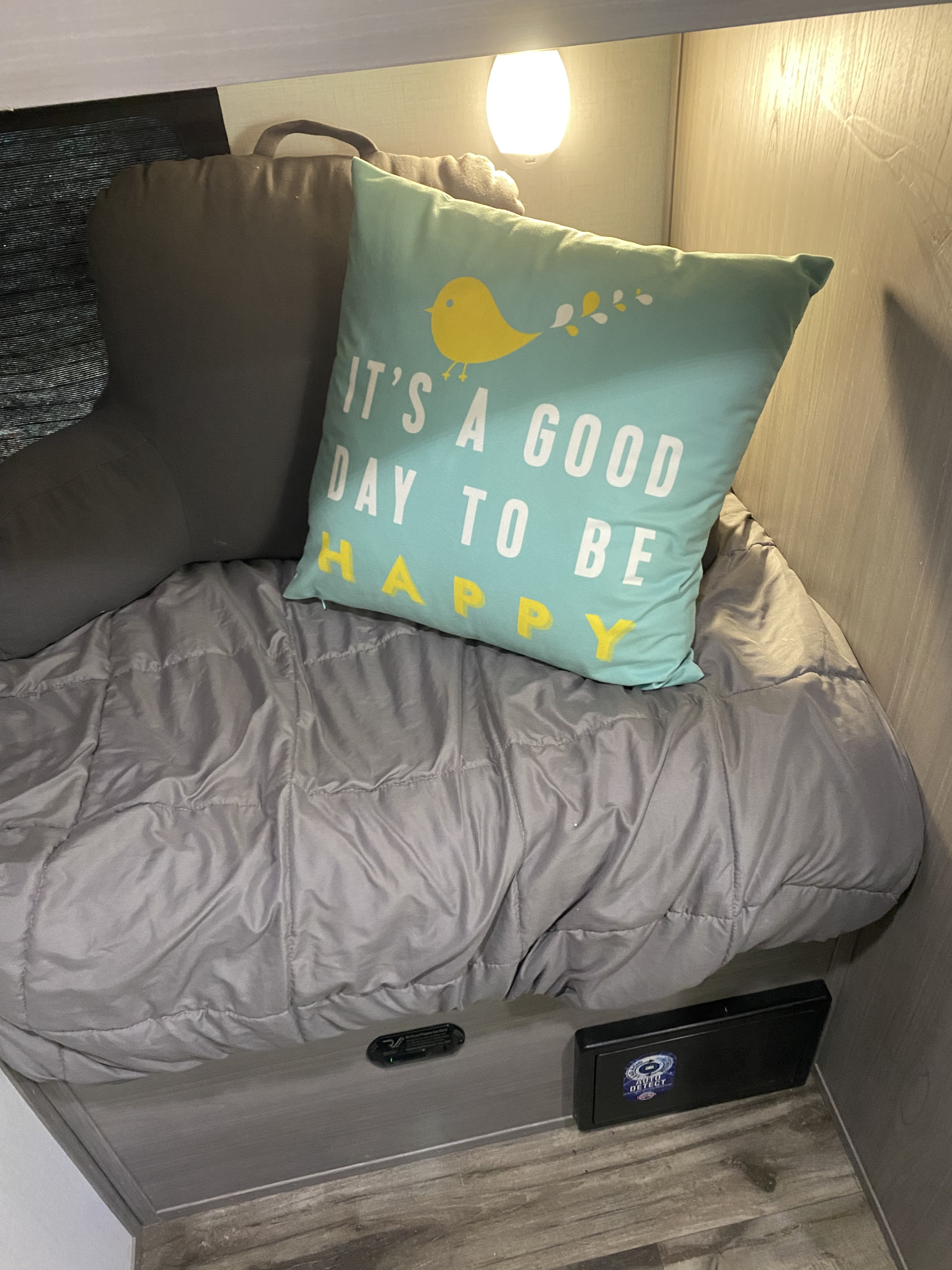An RV rental's cozy bunk: grey bed, comfy pillows, light, and a safety device for restful travels.. Dutchmen 17b 2024