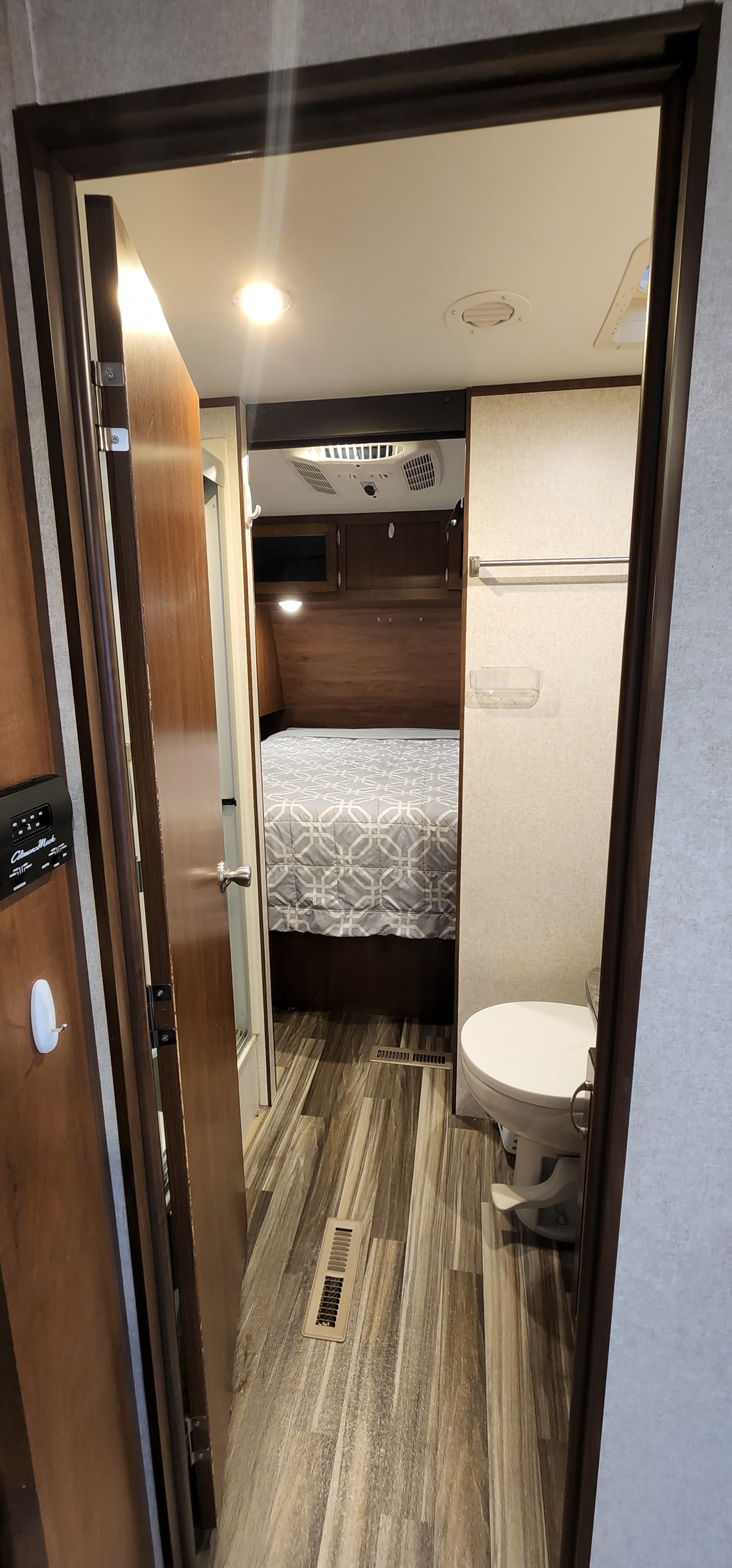 Looking into an RV rental, showing a cozy bedroom with a patterned bed, AC unit, and a small bathroom with a toilet.. Jayco Jay Flight 2017