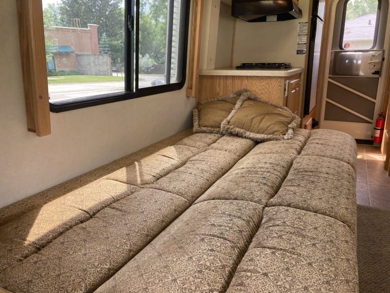 Interior of an RV rental showing a bed/seating area, window view, and compact kitchen.. Born Free Born Free Motorhome 2007