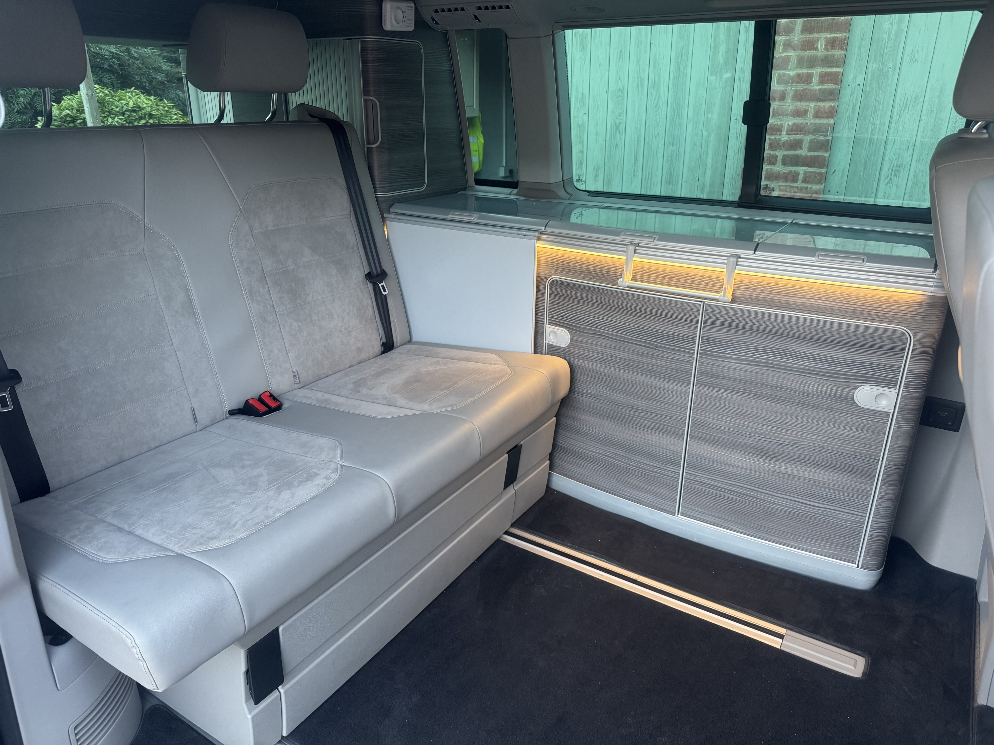Explore a comfortable RV rental interior: grey seating converts to a bed, beside a built-in kitchenette and storage with ambient lighting.. Volkswagen california 2018