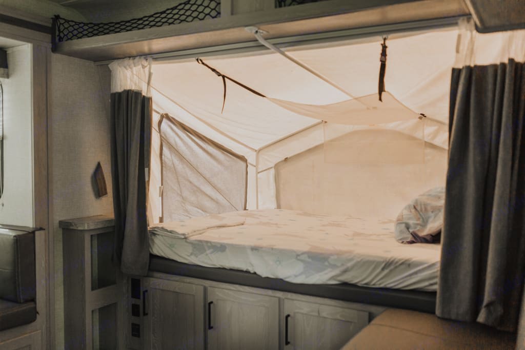 Explore this RV rental's cozy pop-out bed, featuring light canvas walls, curtains, and under-bed storage.. Forest River Flagstaff Shamrock 2022