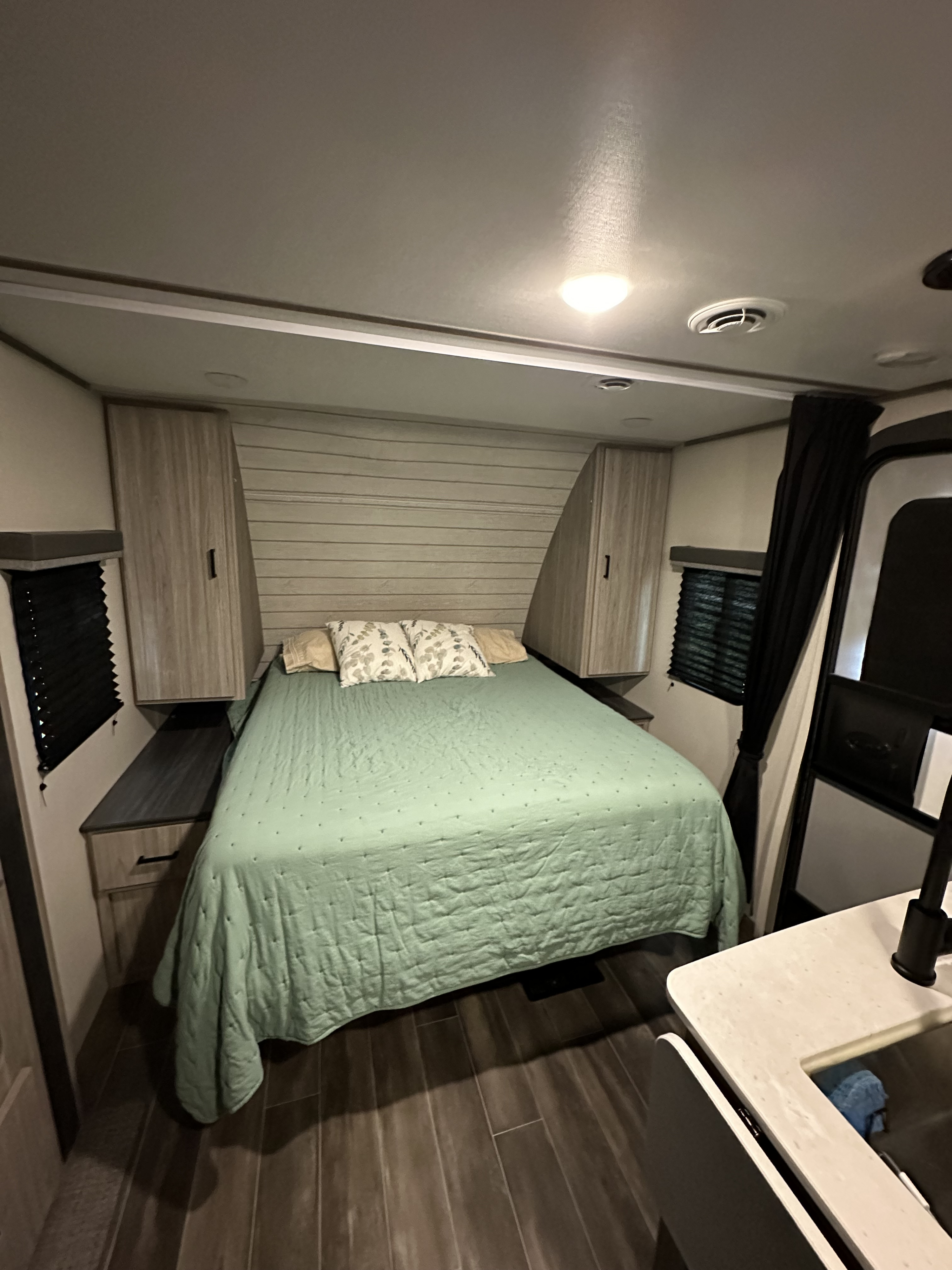 Comfortable RV rental bedroom: light green bedspread, wood paneling, side storage, and ceiling lights.. Keystone RV Passport SL 2022