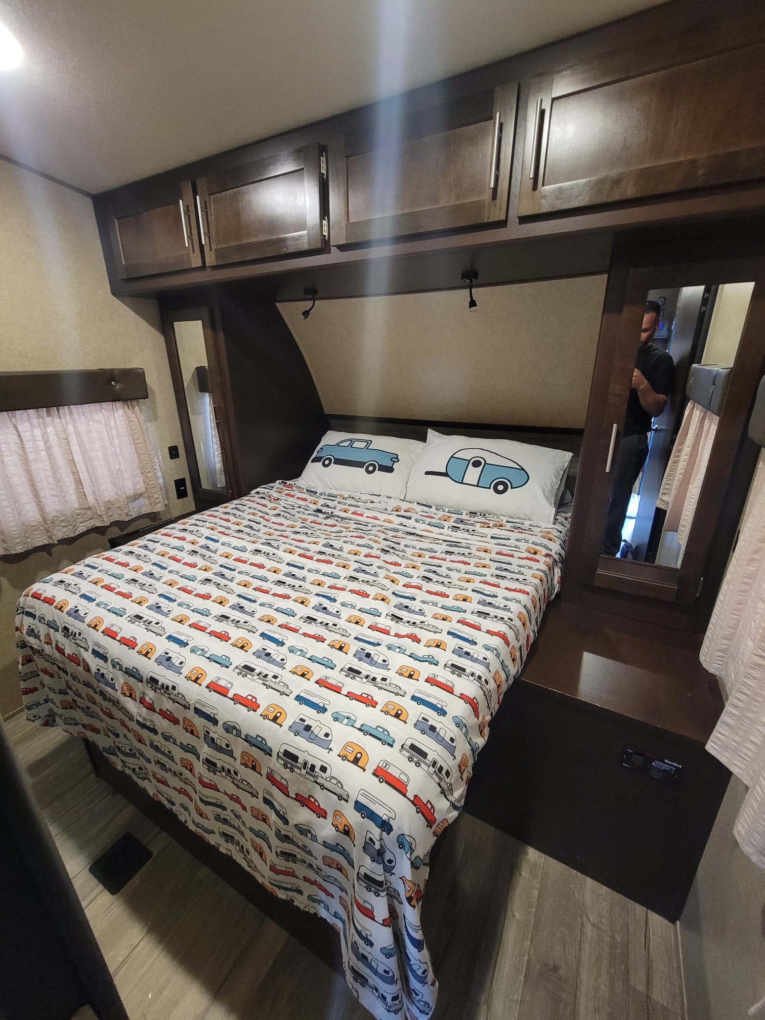 RV rental bedroom featuring a bed with cute car/camper bedding, dark wood cabinets, and a side mirror. Perfect for trips.. Forest River Cherokee Wolf Pack 2018