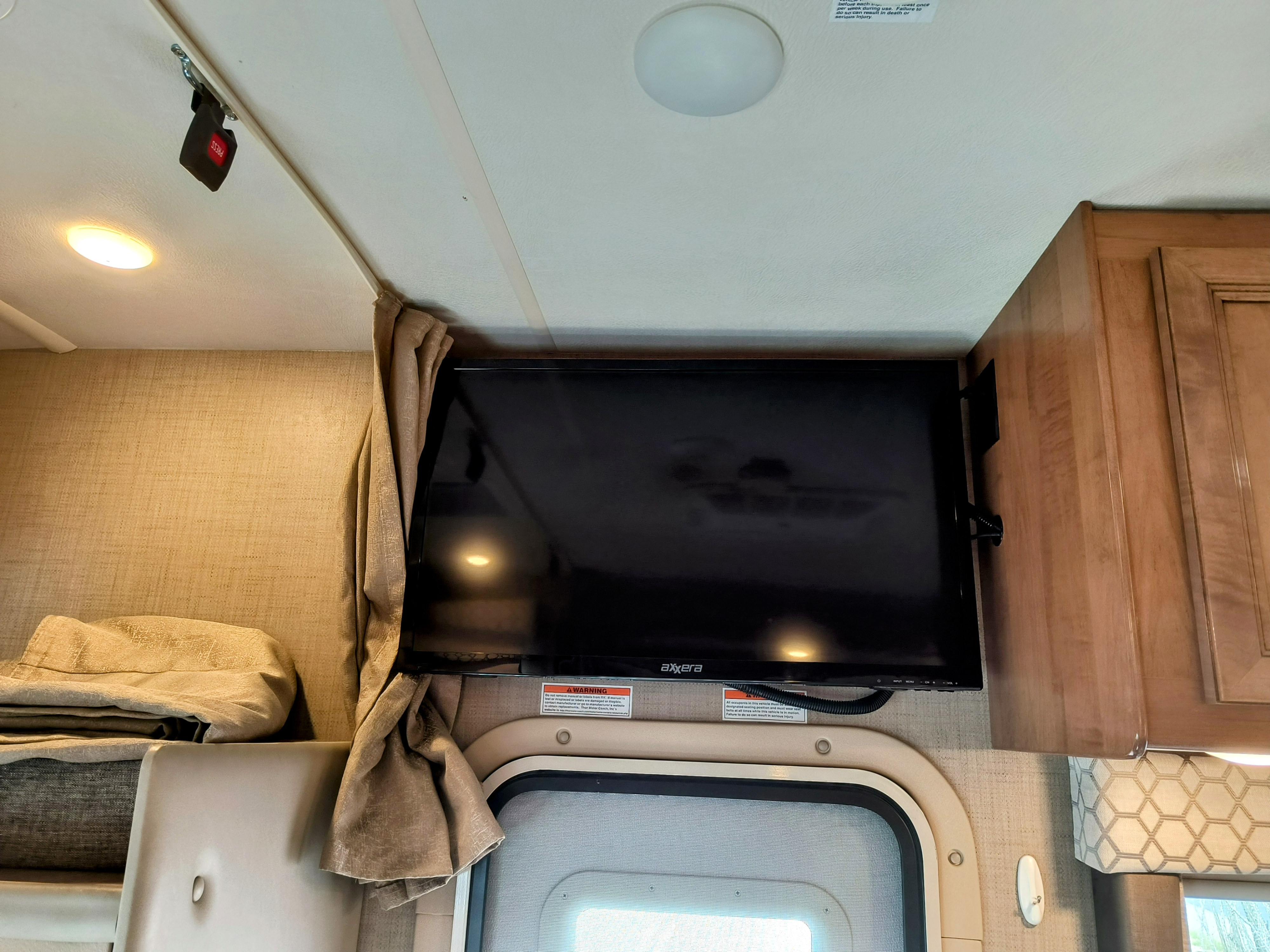 Inside an RV rental: wall-mounted TV, wood cabinets, and bunk. Safety warnings are visible, ensuring a secure journey.. Thor Motor Coach quantum 2020