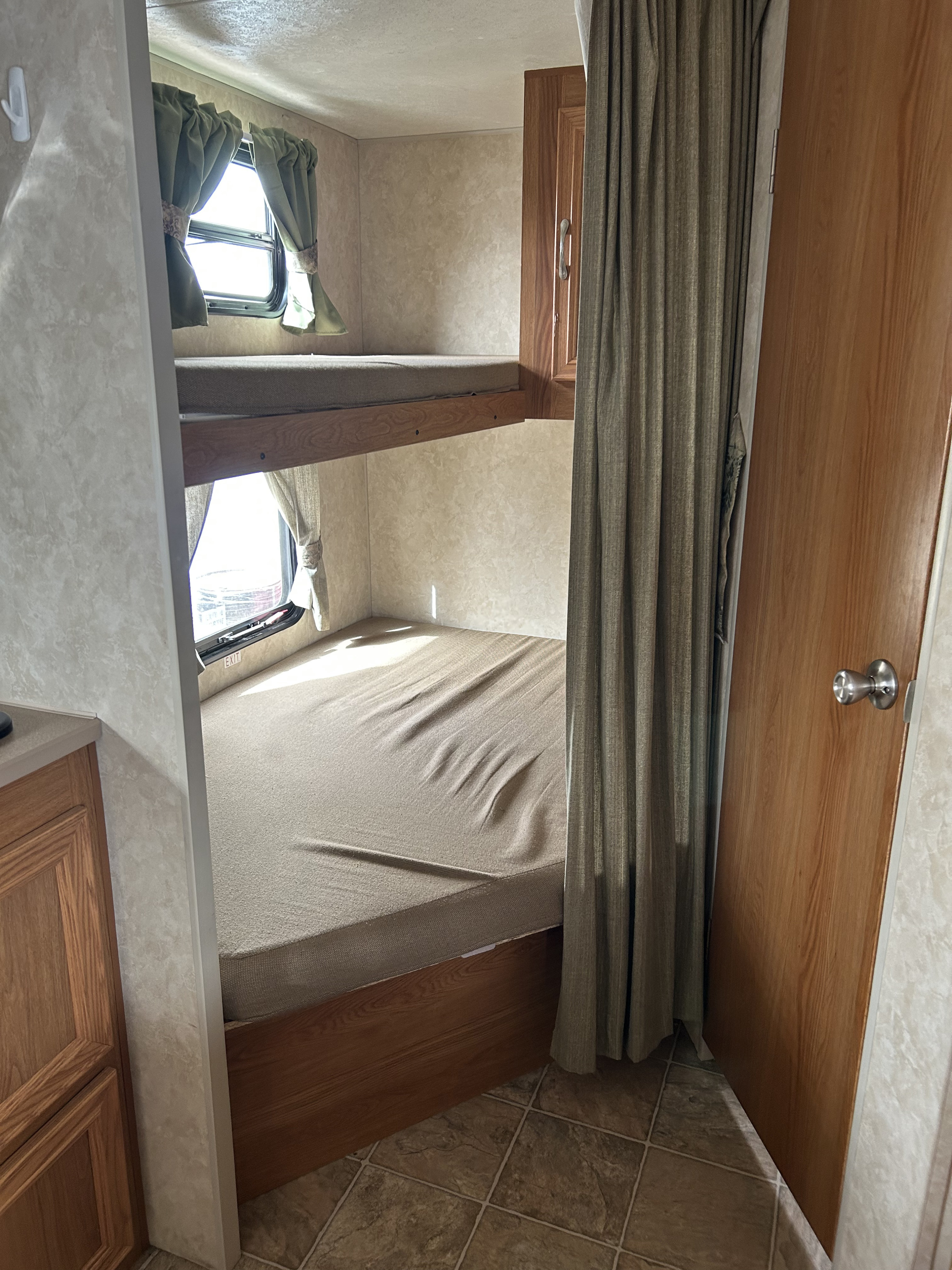 This RV rental shows cozy bunk beds with mattresses, small windows with curtains, a wooden cabinet & door, and tiled floor.. Jag Jag II 2007