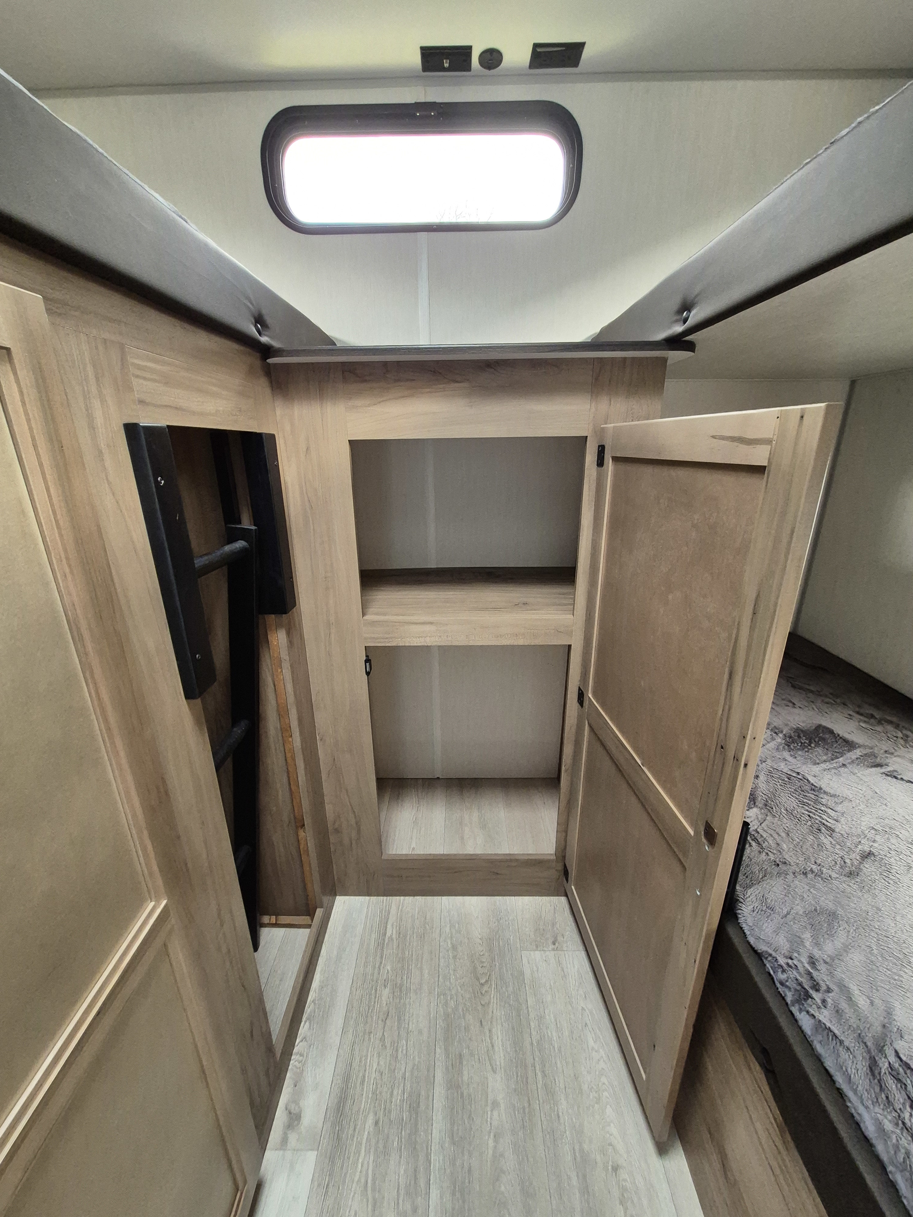 RV rental interior. Built-in storage, a neatly tucked bunk ladder, and a bed with soft, gray bedding provide comfort.. Forest River Cherokee Grey Wolf 29te 2025