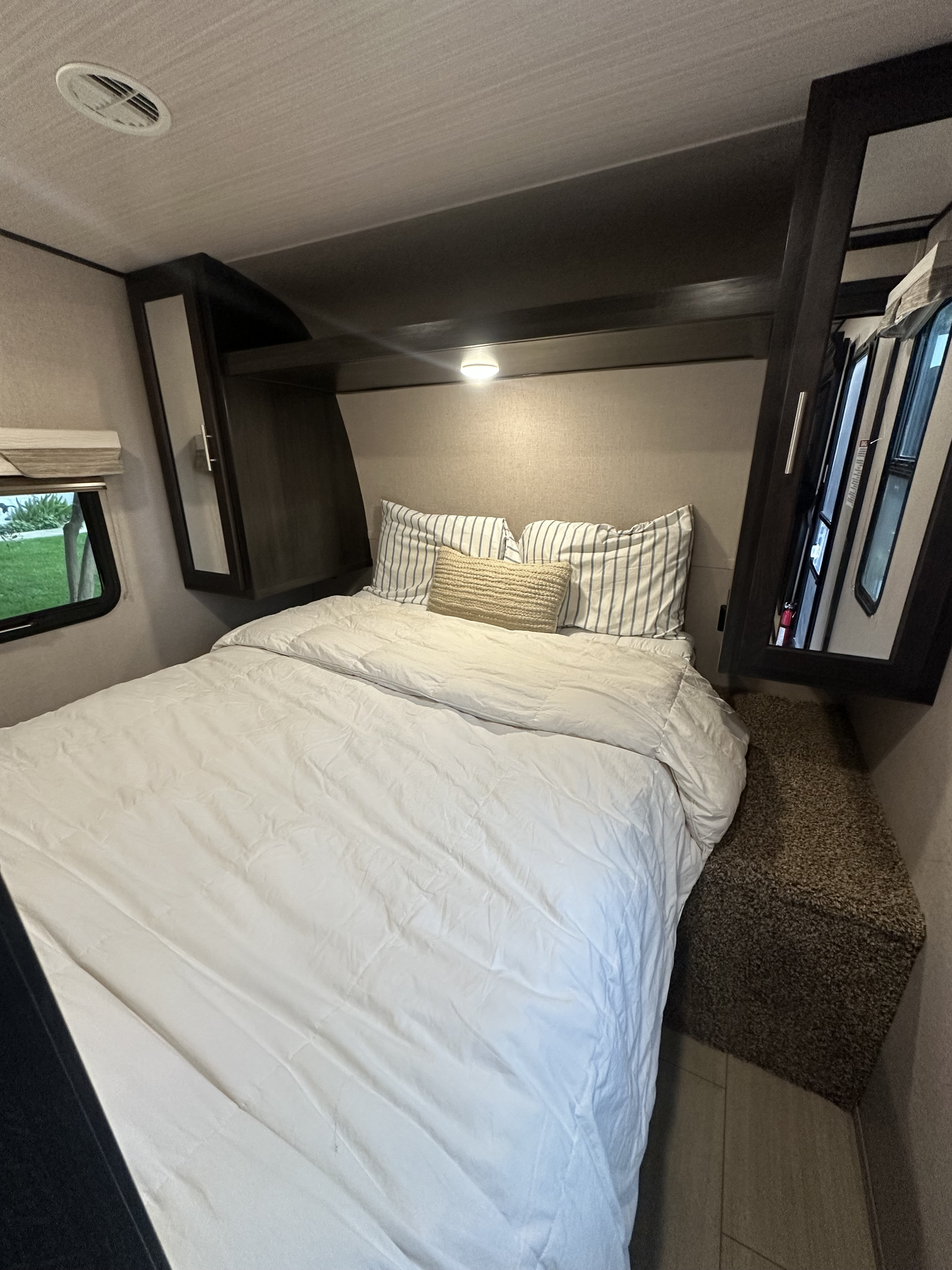 Cozy RV rental bedroom featuring a comfortable bed, striped pillows, overhead storage, and a window with a view outside.. Forest River X-Lite 2017