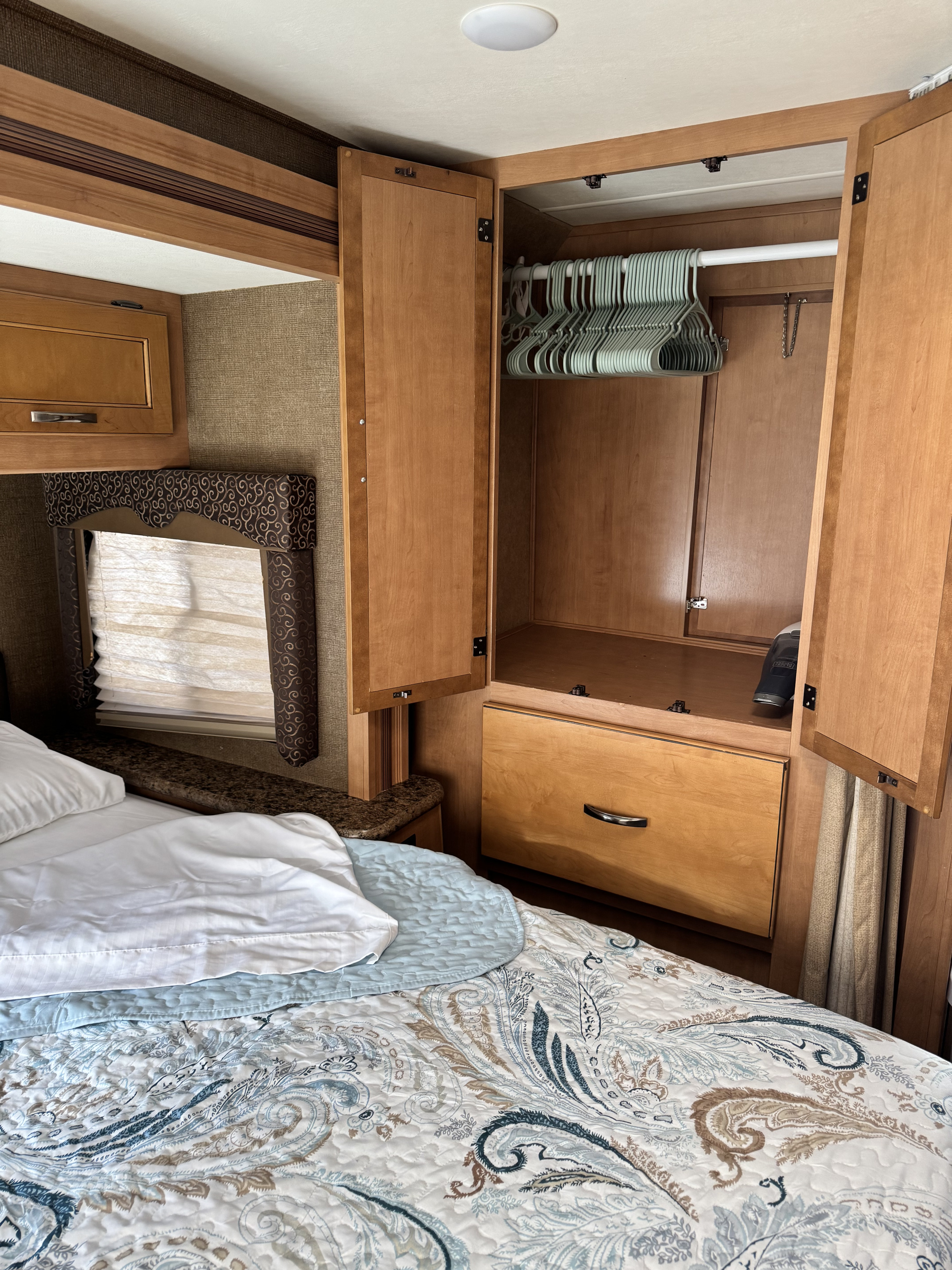 RV rental bedroom interior featuring an open wood wardrobe with empty hangers, a lower drawer, and a light-patterned bed.. Thor Freedom Elite 2016