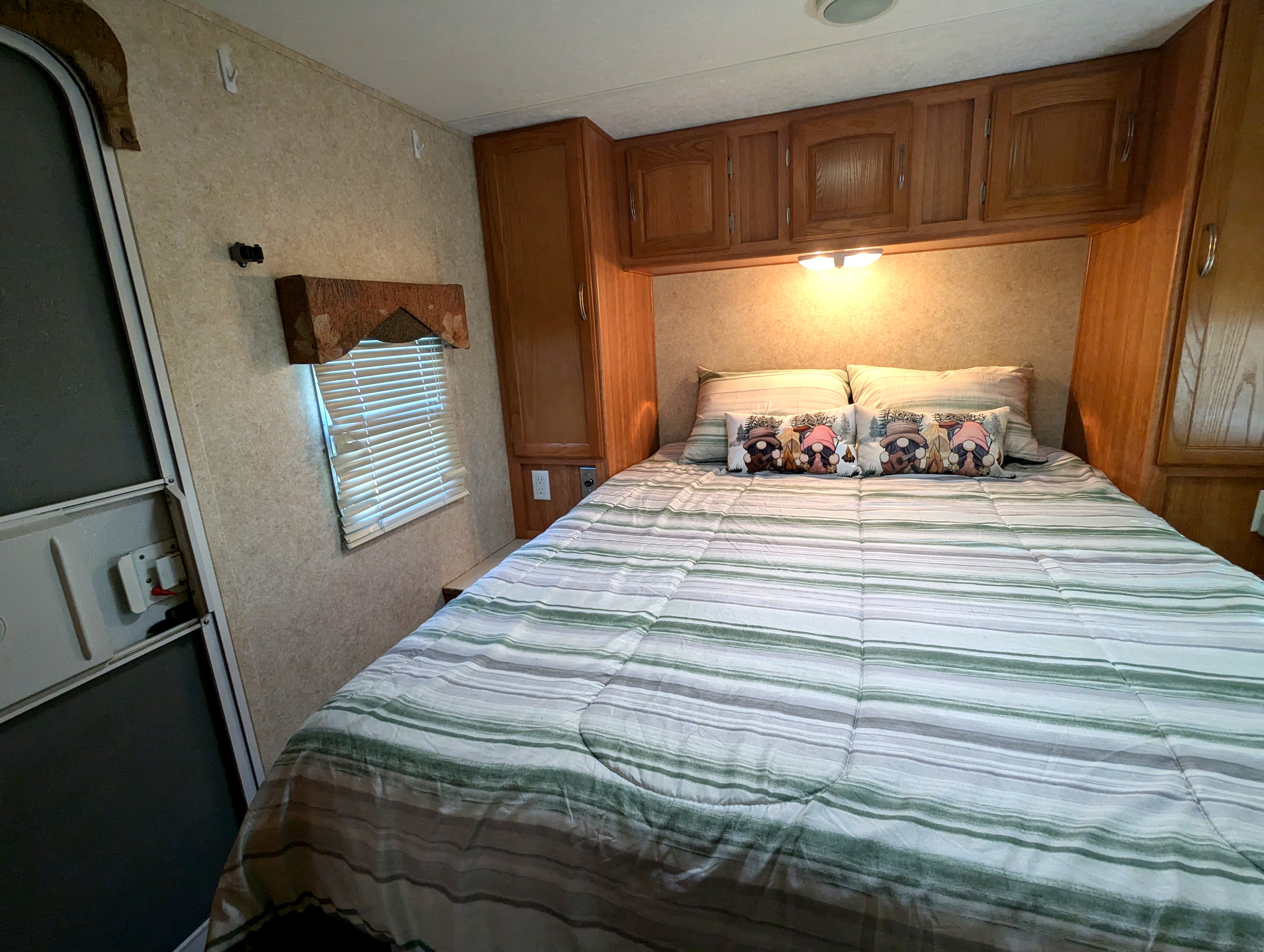 Cozy RV rental bedroom with striped bedding, wooden overhead cabinets, and soft lighting – ideal for travel.. Keystone RV Zeppelin Z-II 2006