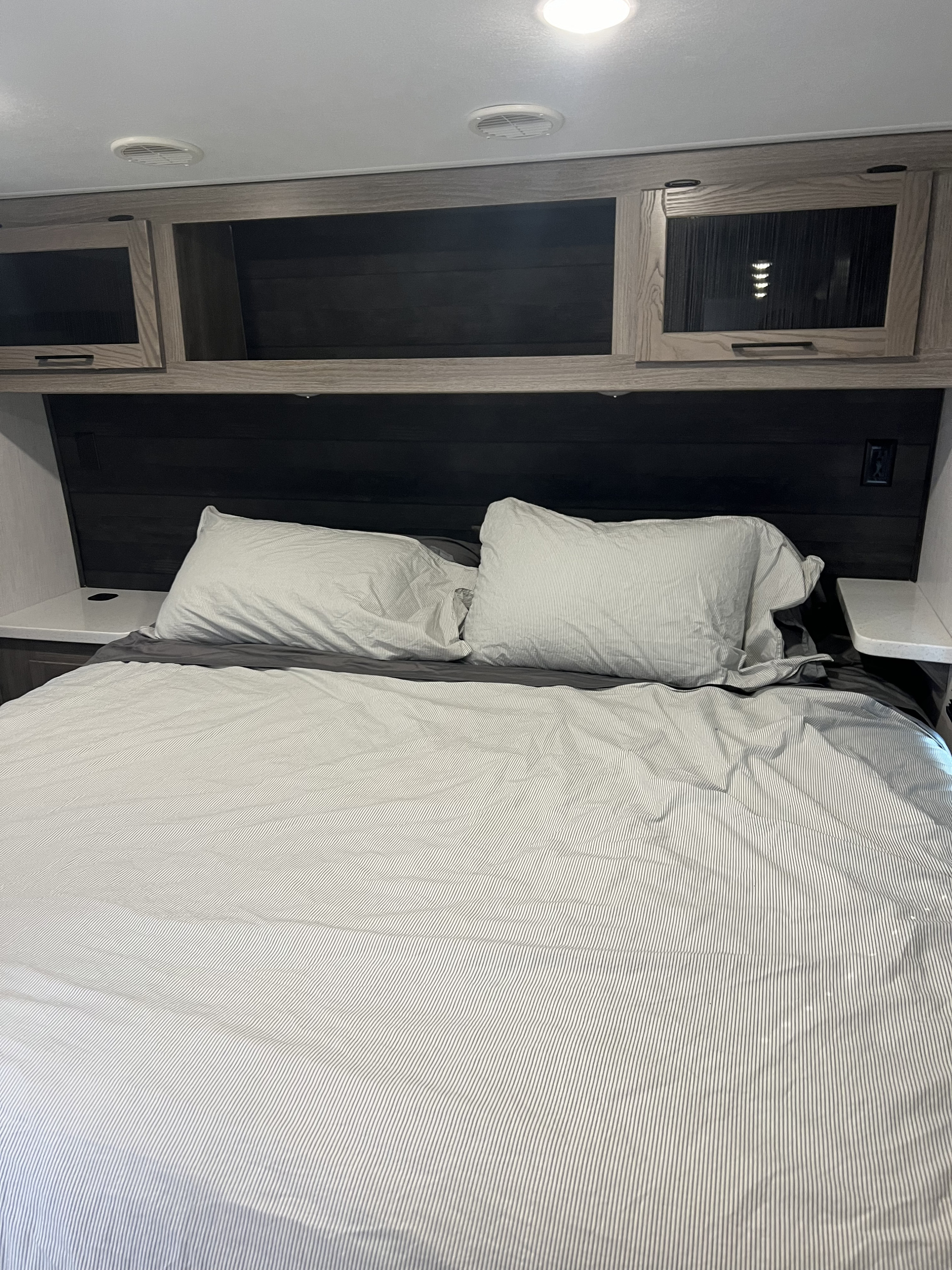 Modern RV rental bedroom with striped bedding, ample overhead cabinets, and practical bedside shelves.. Heartland RVs Fuel Toy Hauler 2022