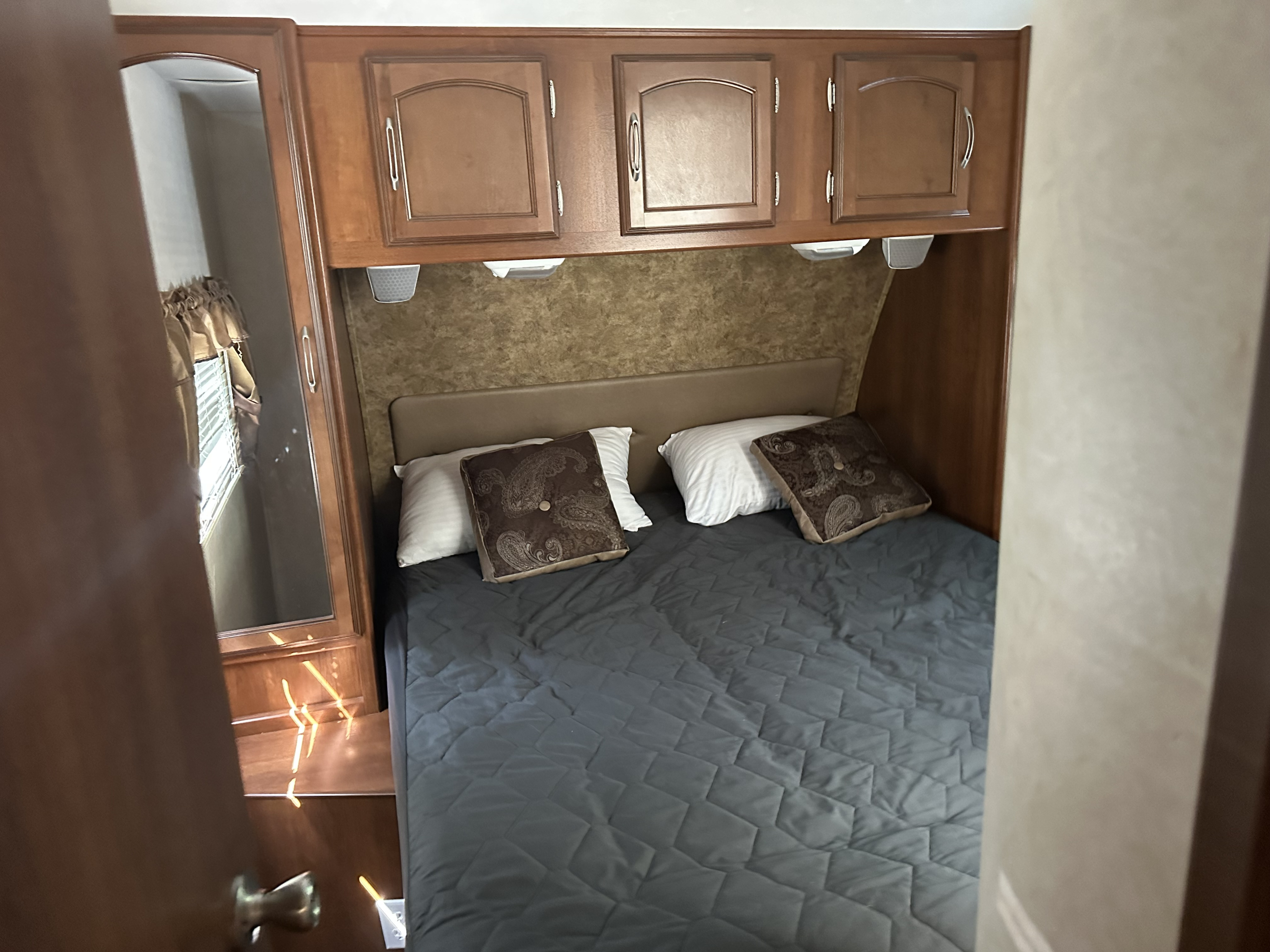 Cozy RV rental bedroom with a comfy bed, overhead cabinets, and a mirrored wardrobe reflecting a window.. Coachmen Freedom Express Liberty Edition 320BHDS 2014