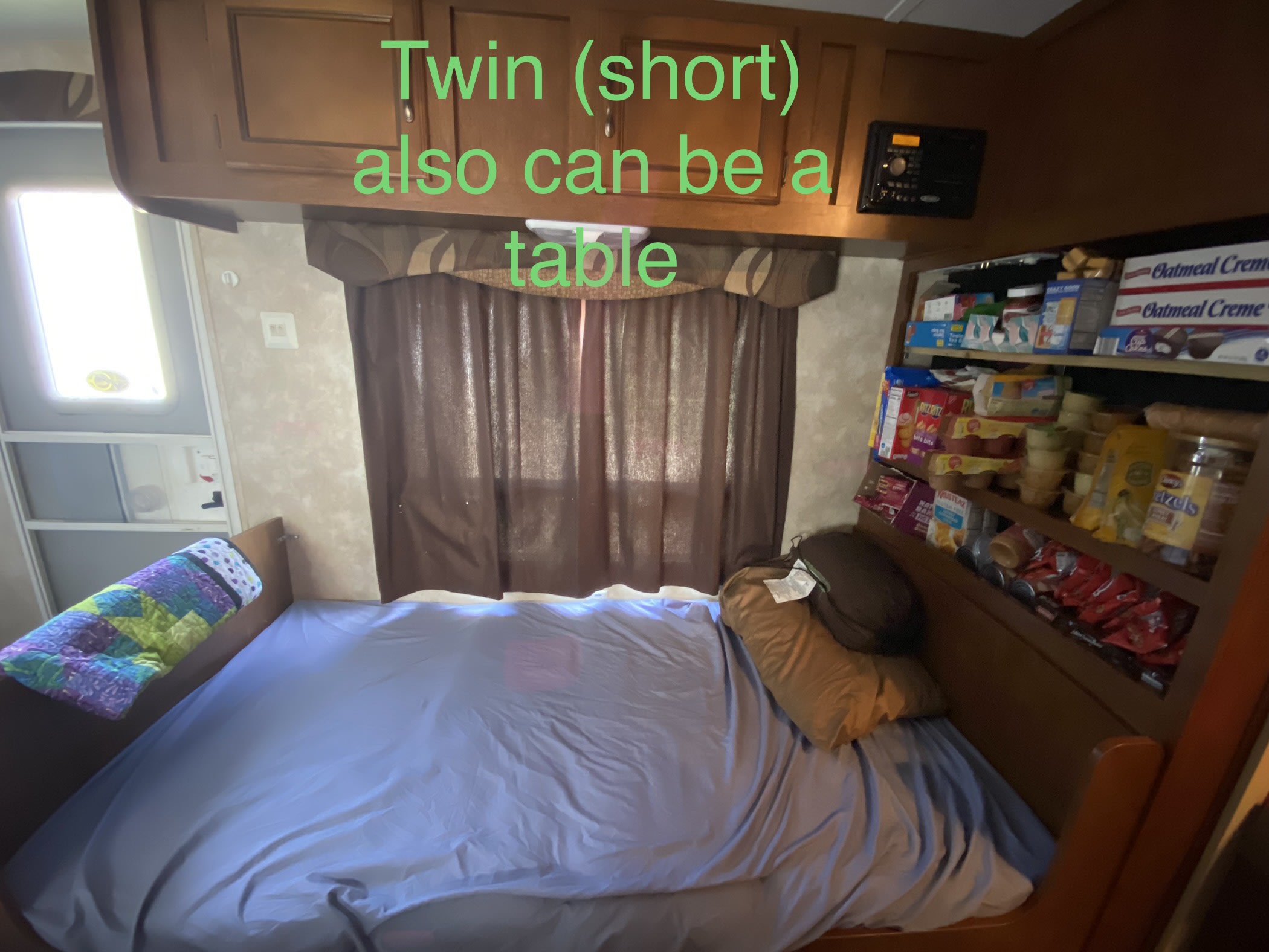 RV rental: A compact interior with wooden cabinets, featuring a convertible twin bed, window, and well-stocked snack shelves.. Coachmen catalina 2013