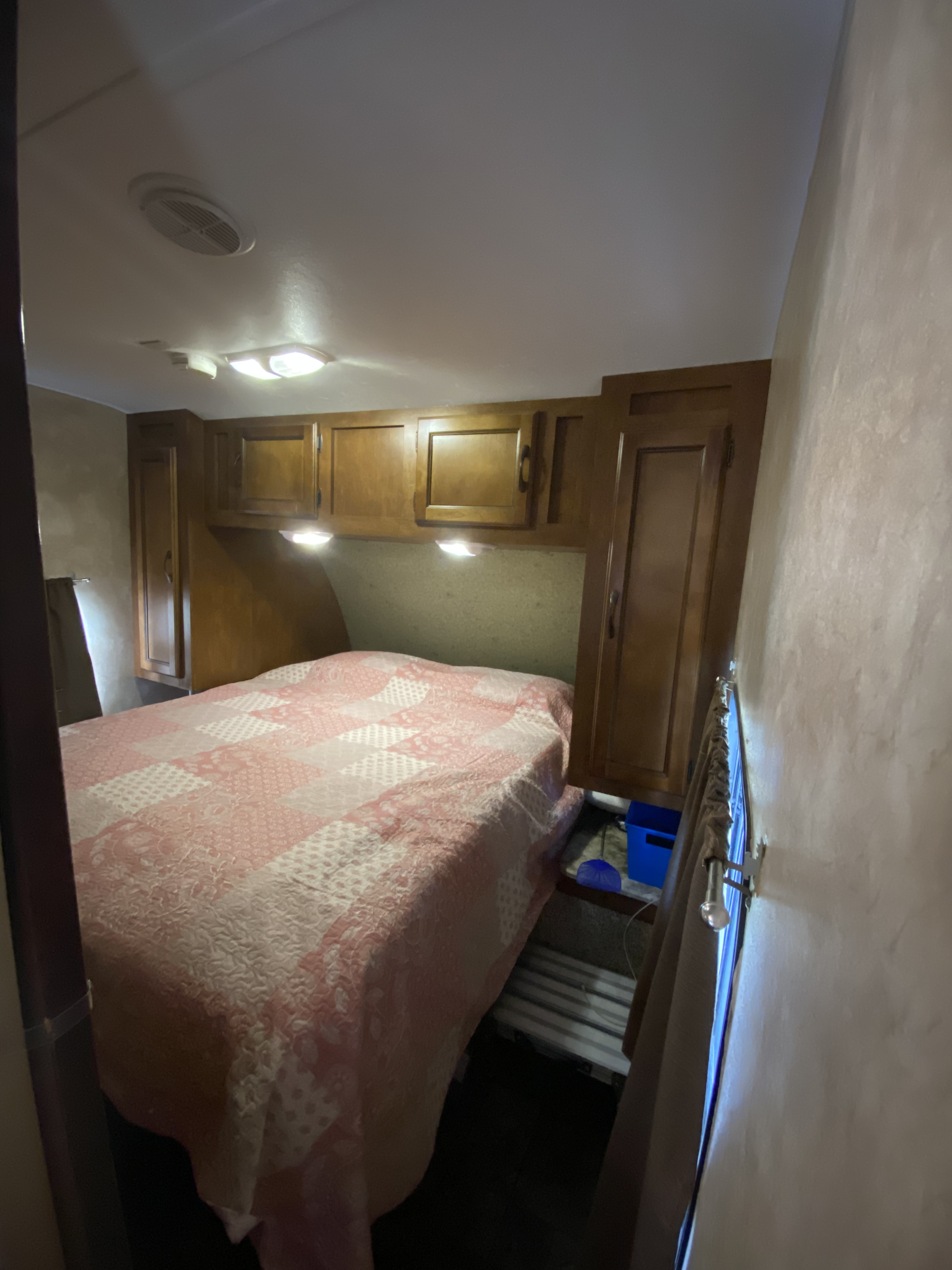 Cozy RV rental bedroom featuring a patterned bed, wood overhead cabinets, and bright ceiling lights, ready for your travels.. Coachmen catalina 2013