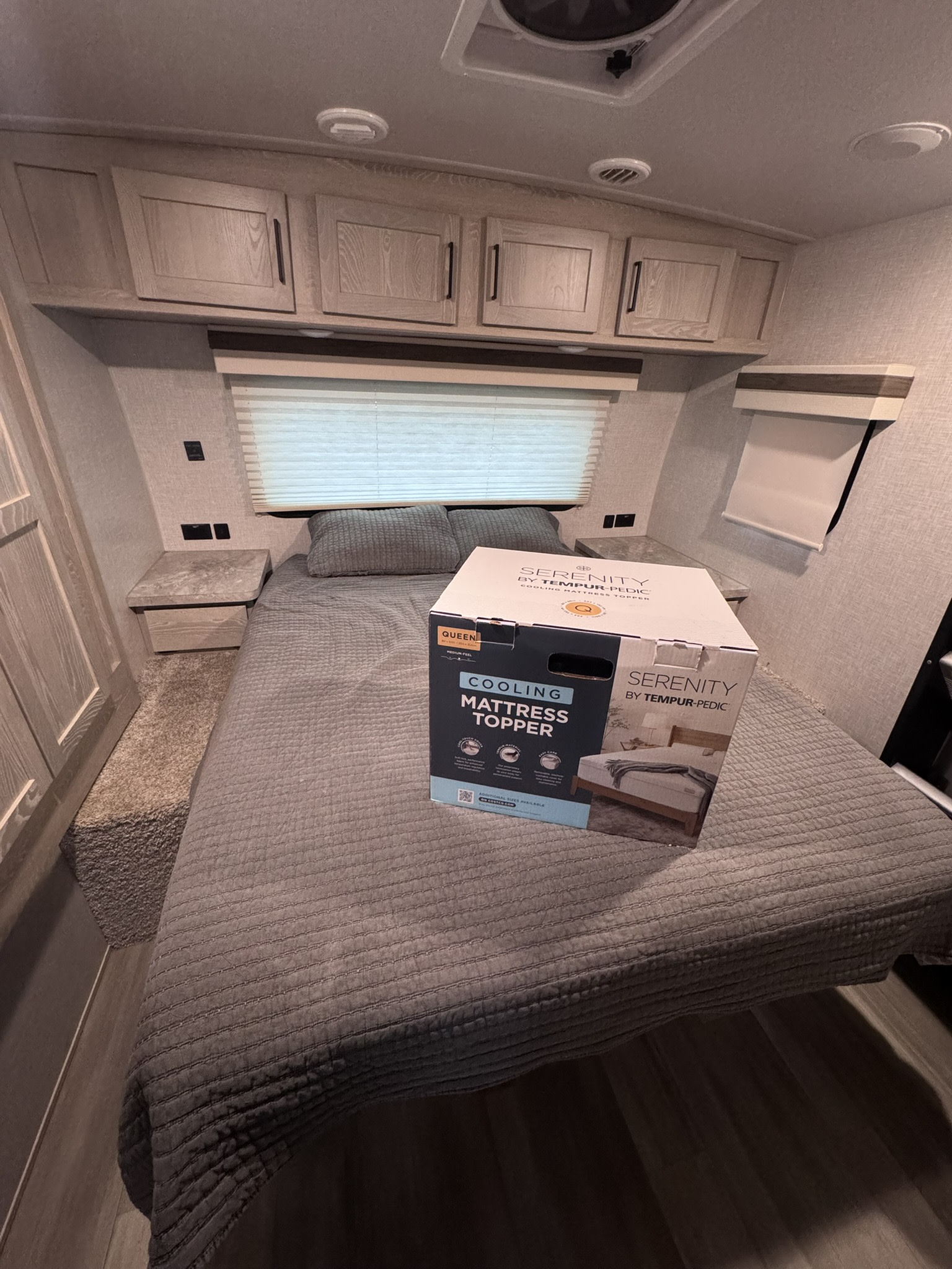 RV rental bedroom with a Serenity by Tempur-Pedic Cooling Mattress Topper box on the queen bed, featuring overhead cabinets and a window.. Forest River Rockwood Ultra Lite 2022