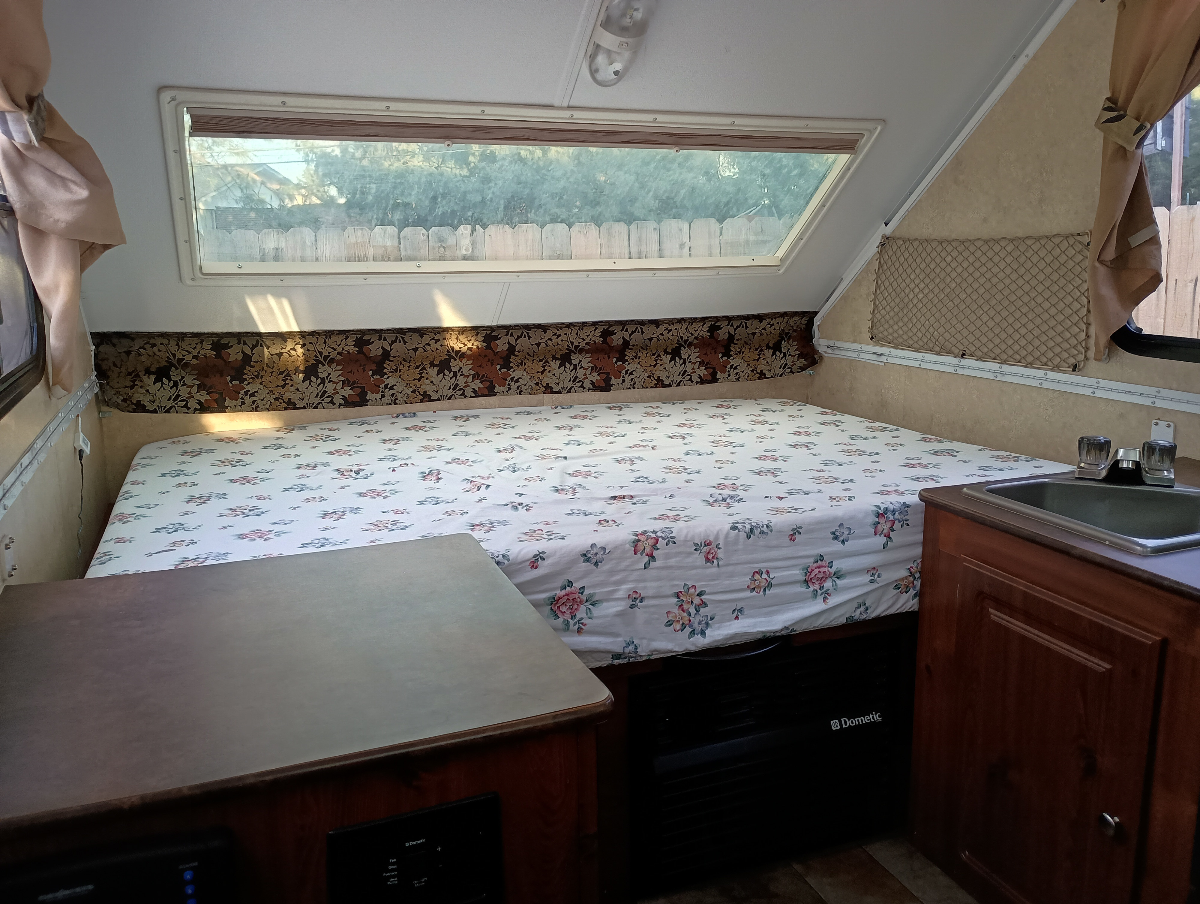 Cozy RV rental interior featuring a floral bed, large window view, and a compact kitchenette with a sink.. Forest River Flagstaff Classic 2014
