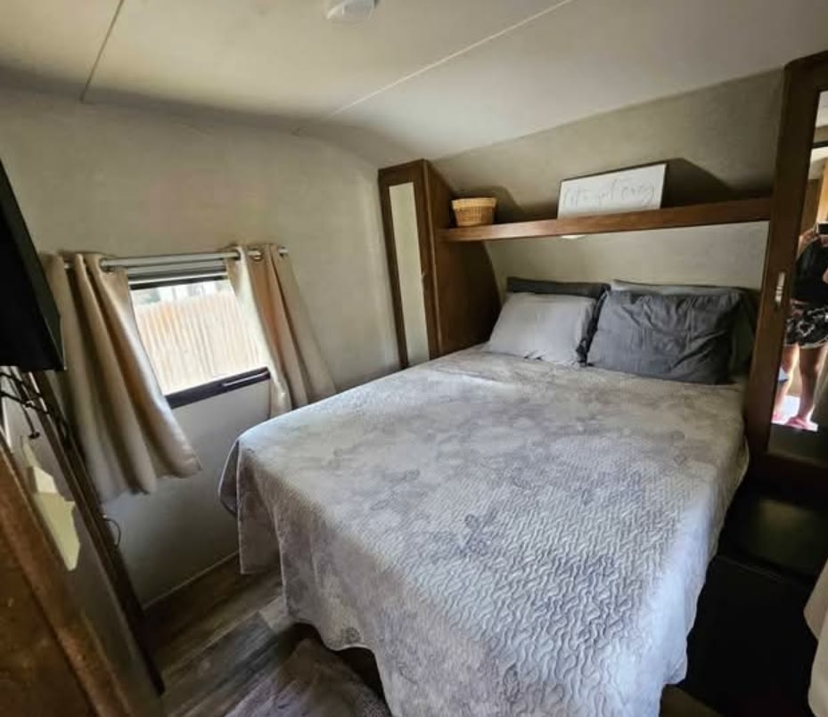 Cozy RV rental bedroom with a light gray patterned quilt on the bed, window with curtains, and an overhead shelf.. Forest River Salem 2017