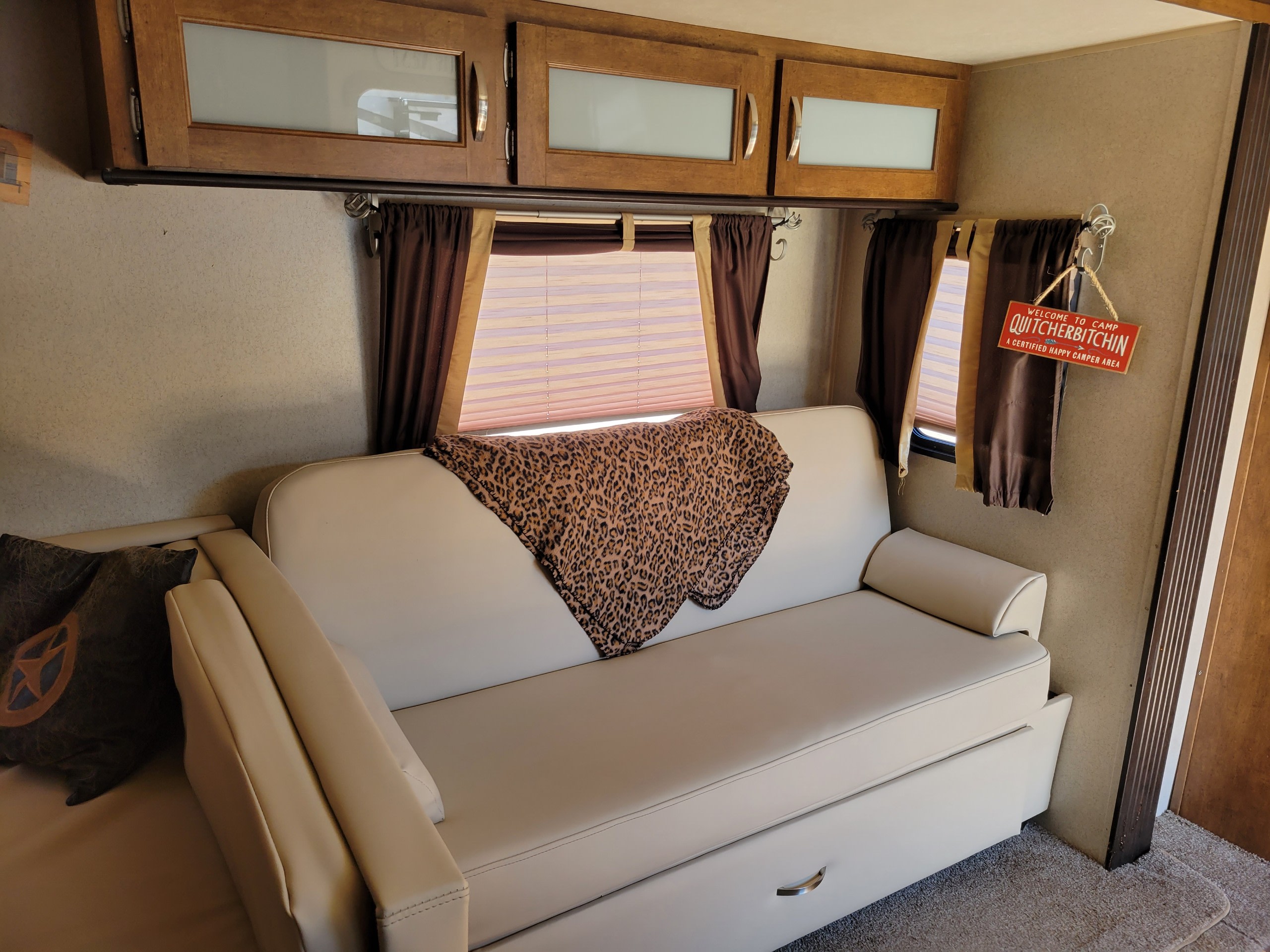 Inviting RV interior features a cream sofa, leopard print blanket, overhead cabinets & a "Camp Quitcherbitchin'" sign. Great for an rv rental.. Forest River Salem 2017