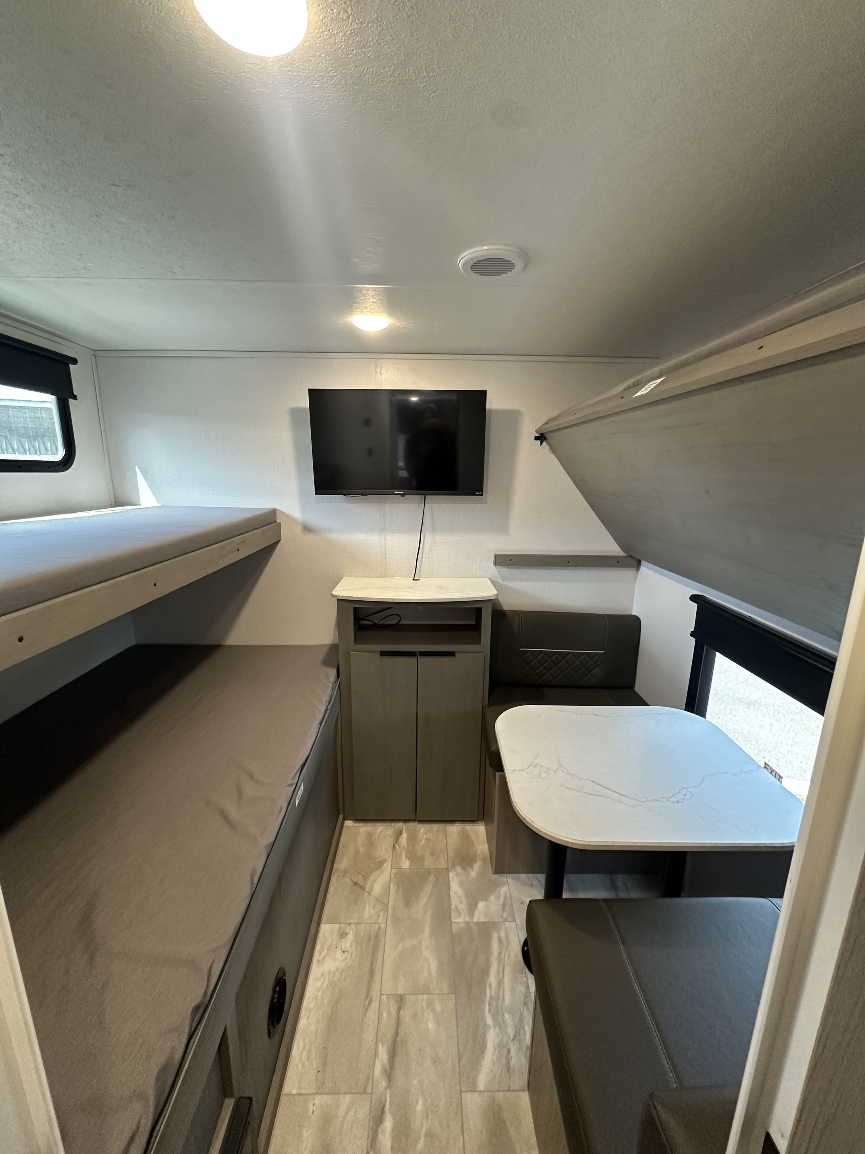 This RV rental interior features comfy bunk beds, a dining area, and a wall-mounted TV, creating a functional living space.. Dutchmen Kodiak SE 2024
