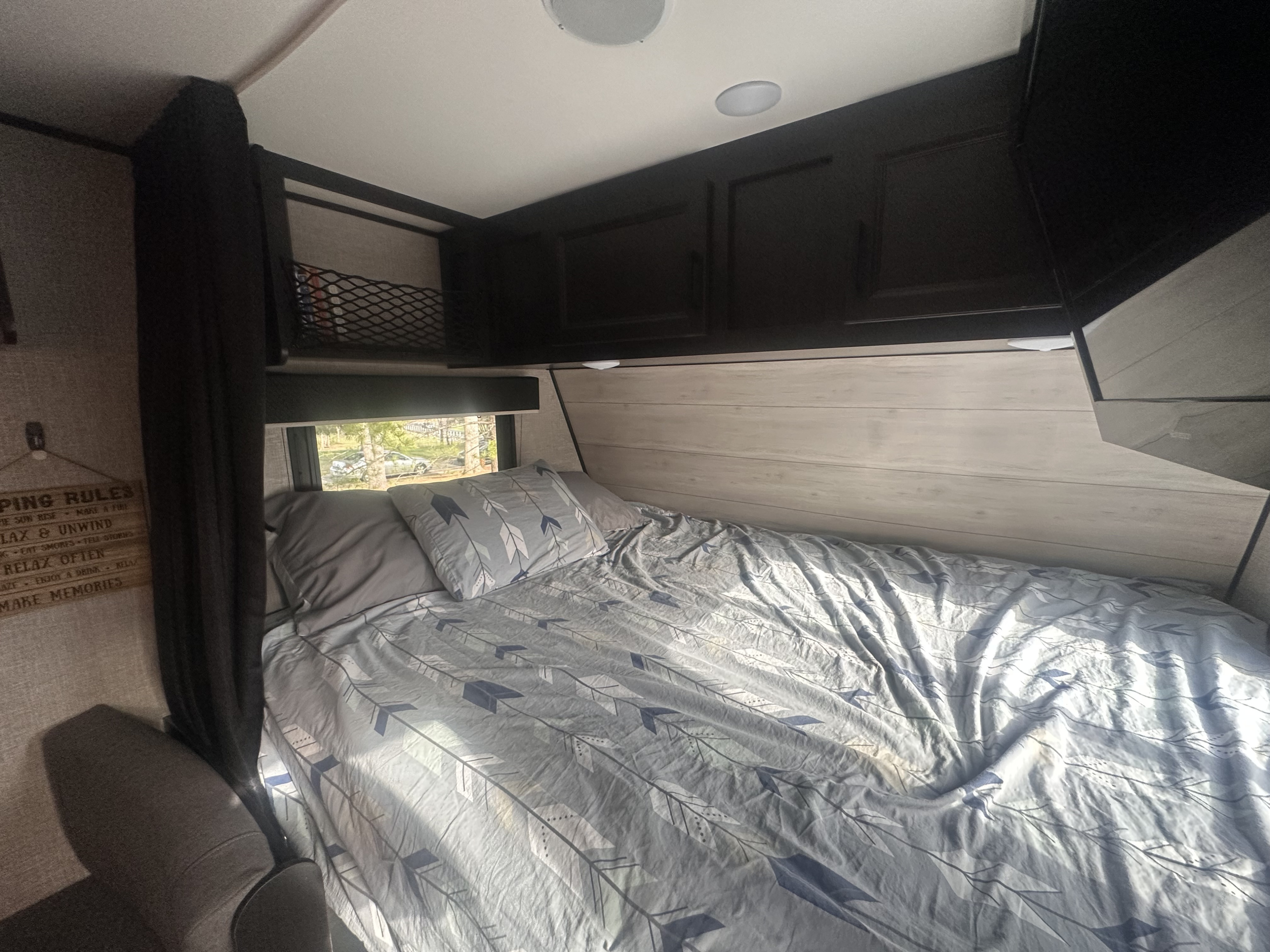 Cozy RV rental bedroom with arrow-patterned bedding, overhead cabinets, and a window view. Perfect for an RV adventure.. Jayco Jay Flight 2022