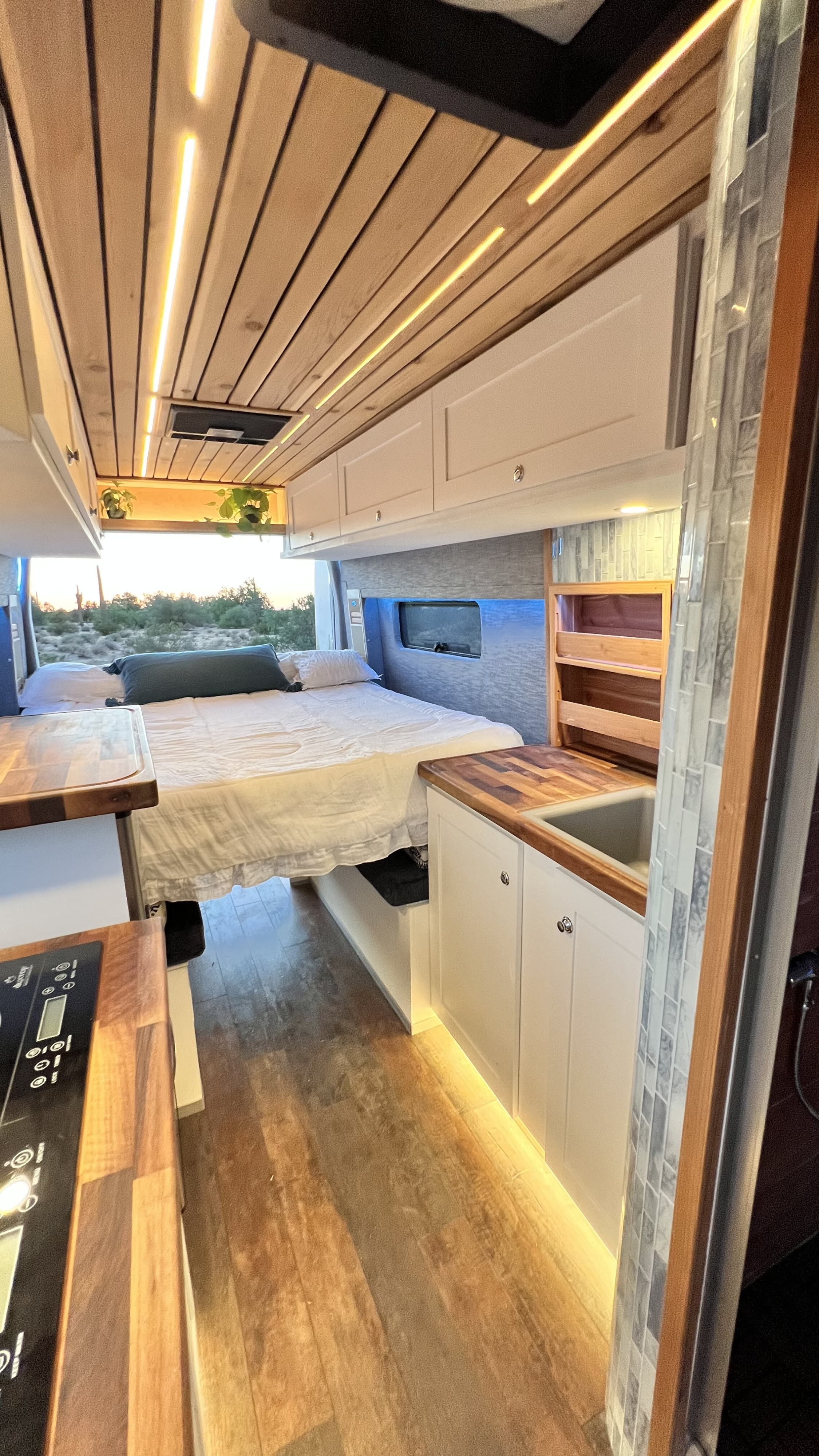 Spacious RV rental interior with a cozy bed, equipped kitchen, wooden ceiling, and warm under-cabinet lighting.. Ford Transit 2019