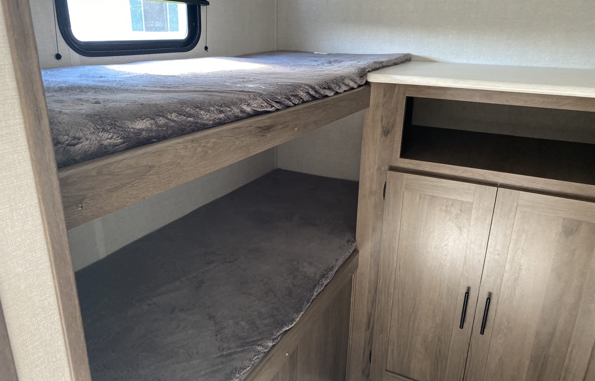 This RV rental features cozy bunk beds with gray blankets & built-in storage cabinets.. Prime Time Avenger 2021