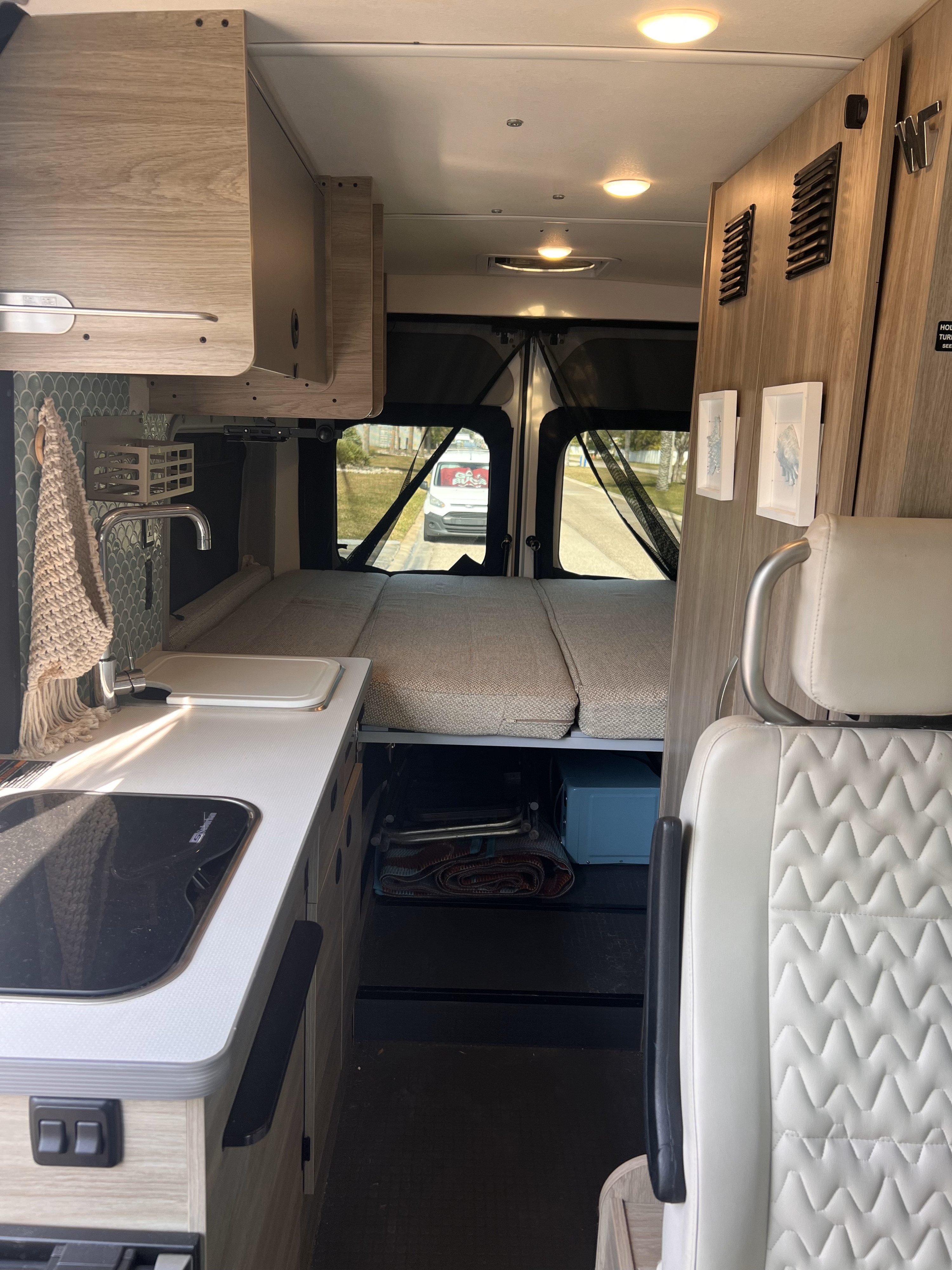 Inside an RV rental camper van, showing the kitchen with sink/stove, bed, and rear view.. Winnebago Solis 59P 2021
