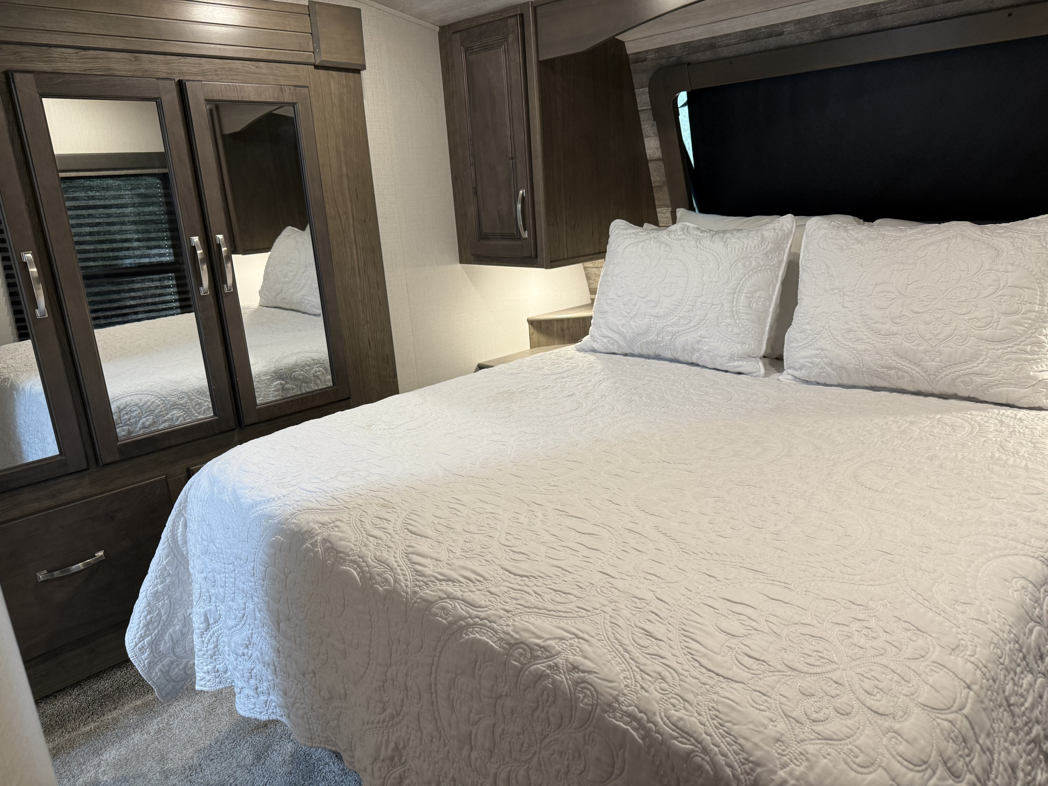 Spacious RV rental bedroom featuring a clean white quilted bed, mirrored wardrobe, and overhead storage.. Keystone RV Cougar 2021