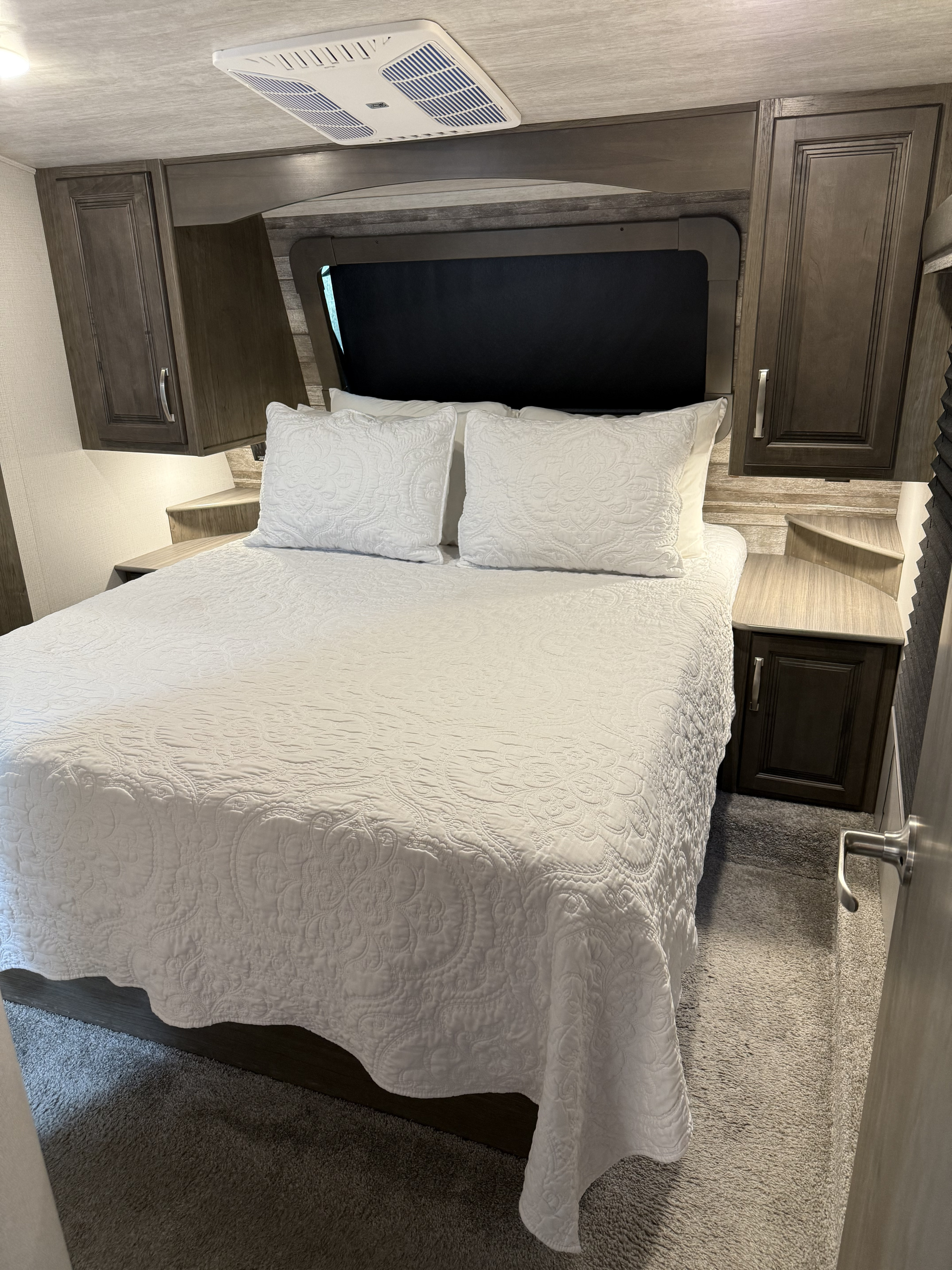 Cozy RV rental bedroom: white bed, integrated nightstands, and overhead AC unit. Ideal for comfortable travel.. Keystone RV Cougar 2021