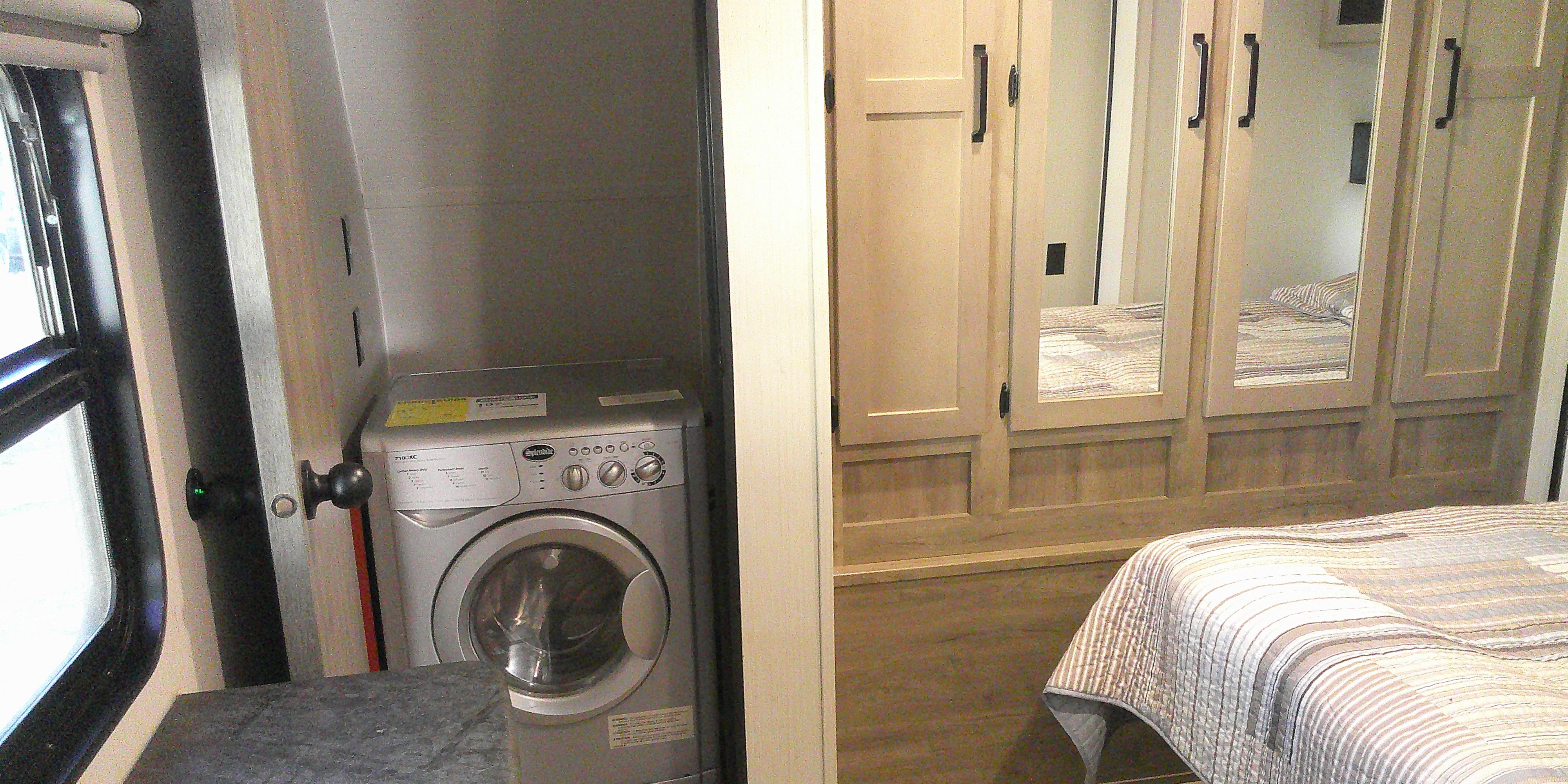 RV rental interior: compact washer/dryer by window, adjacent to a cozy bedroom with mirrored wardrobe.. Puma palomino 2023