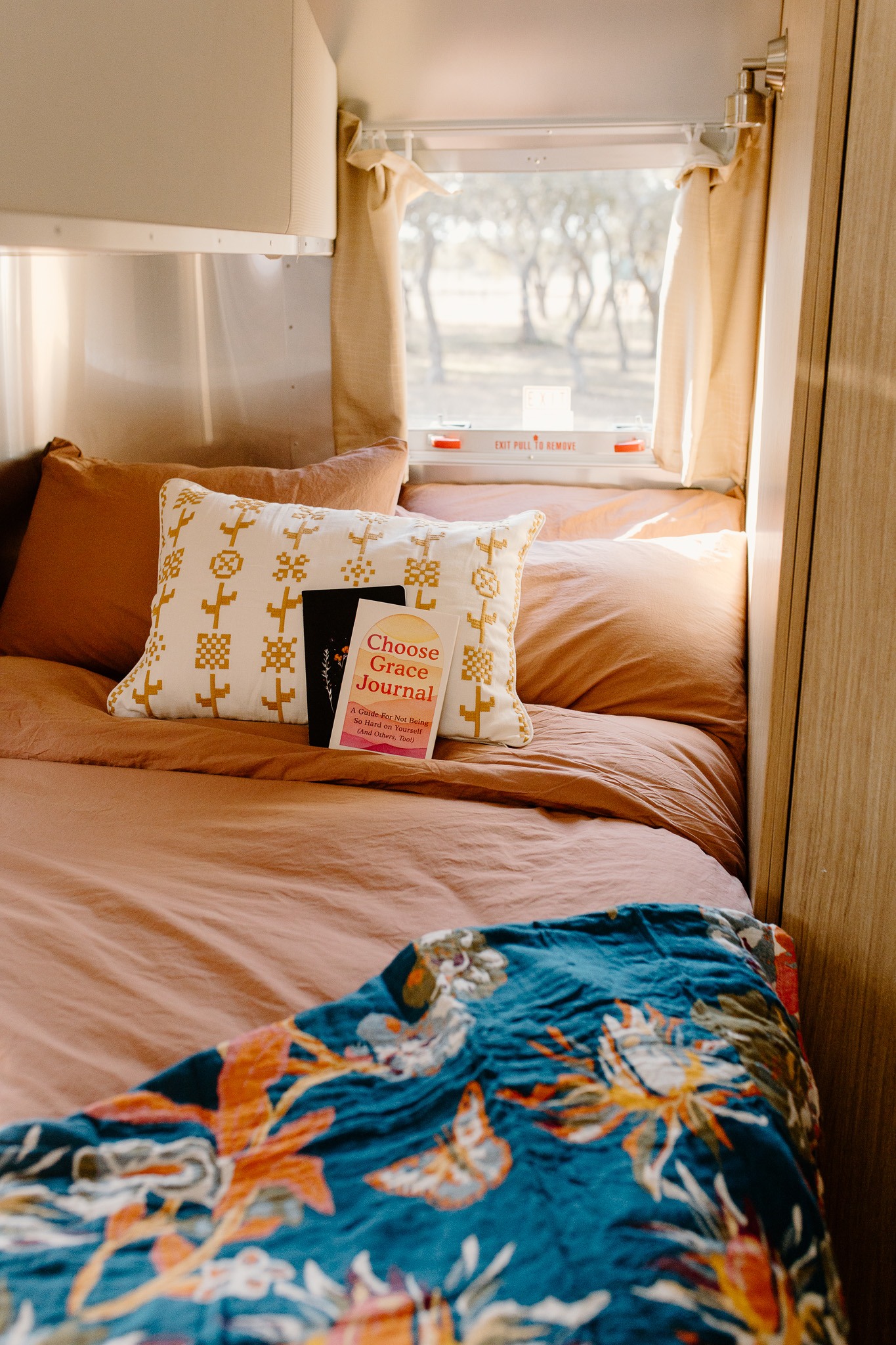 Relaxing rv rental interior. Earthy-toned bed with "Choose Grace Journal" on a patterned pillow and a vibrant blue blanket.. Airstream Flying Cloud 2019