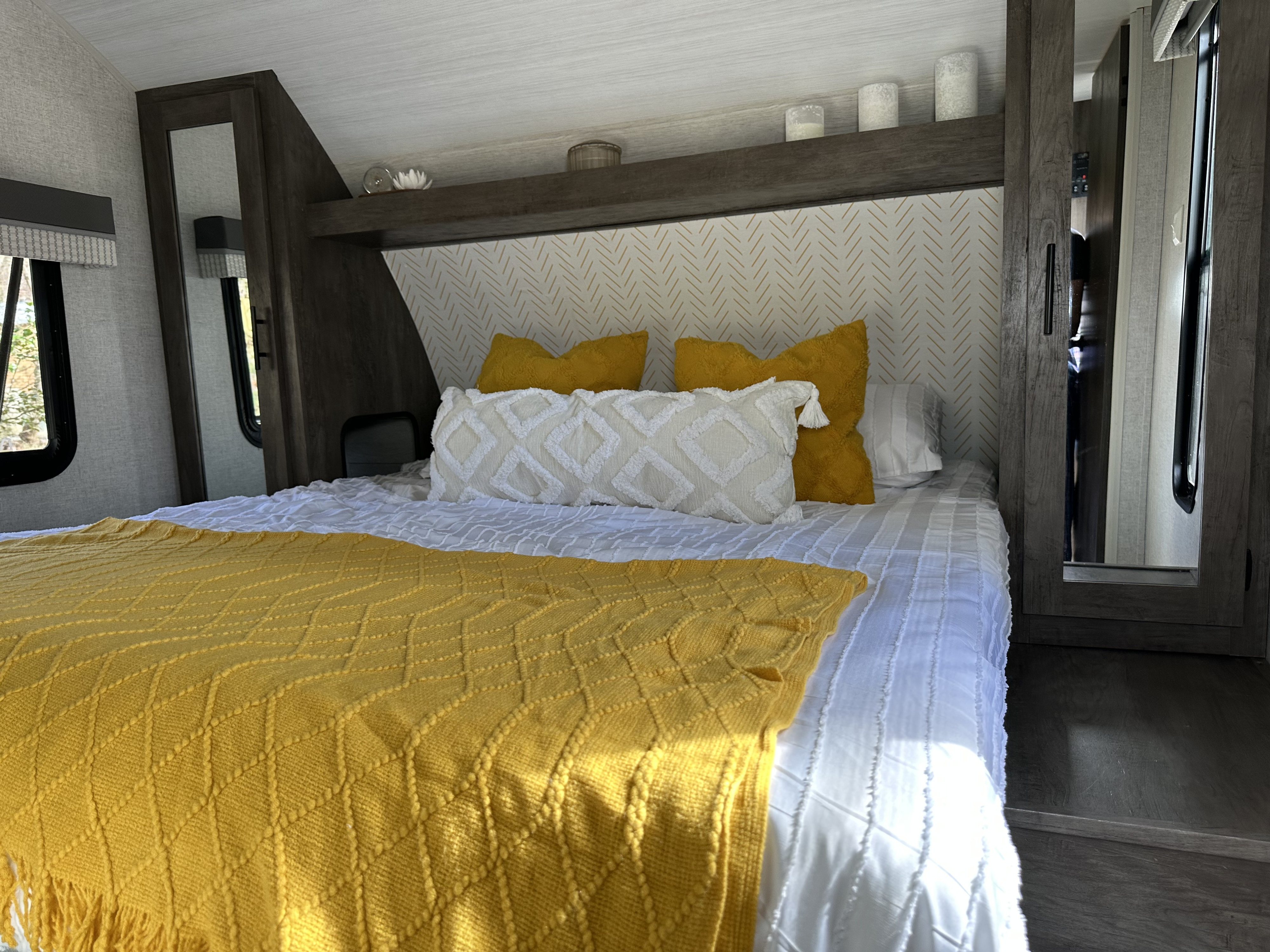 Bright and cozy RV rental bedroom. Yellow and white bedding on bed, patterned headboard, and wood built-in storage.. Forest River Salem Cruise Lite 2021