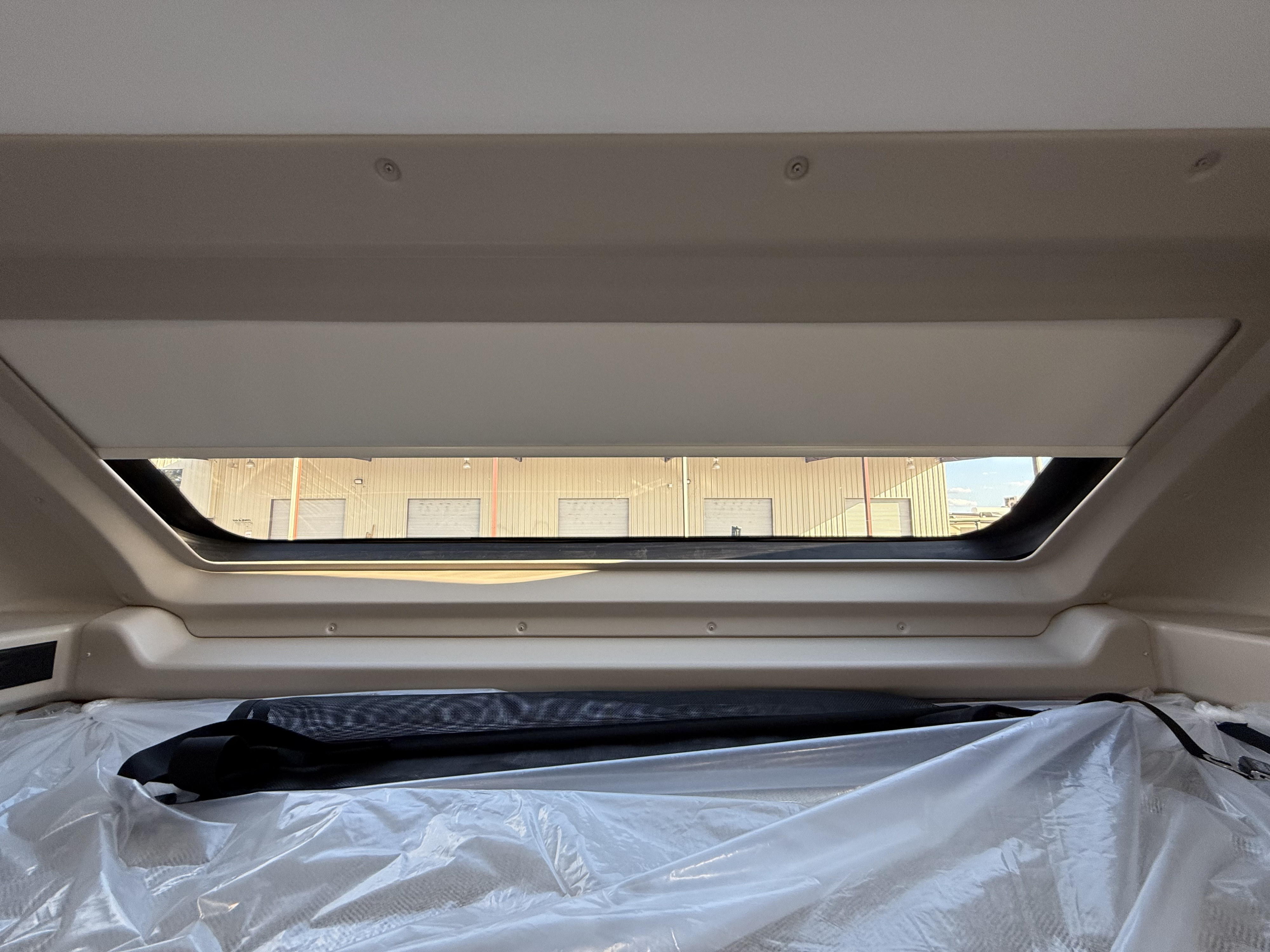 RV rental interior: A protected sleeping bunk with clear plastic, looking out a window at industrial buildings.. Entegra Coach Esteem 2025