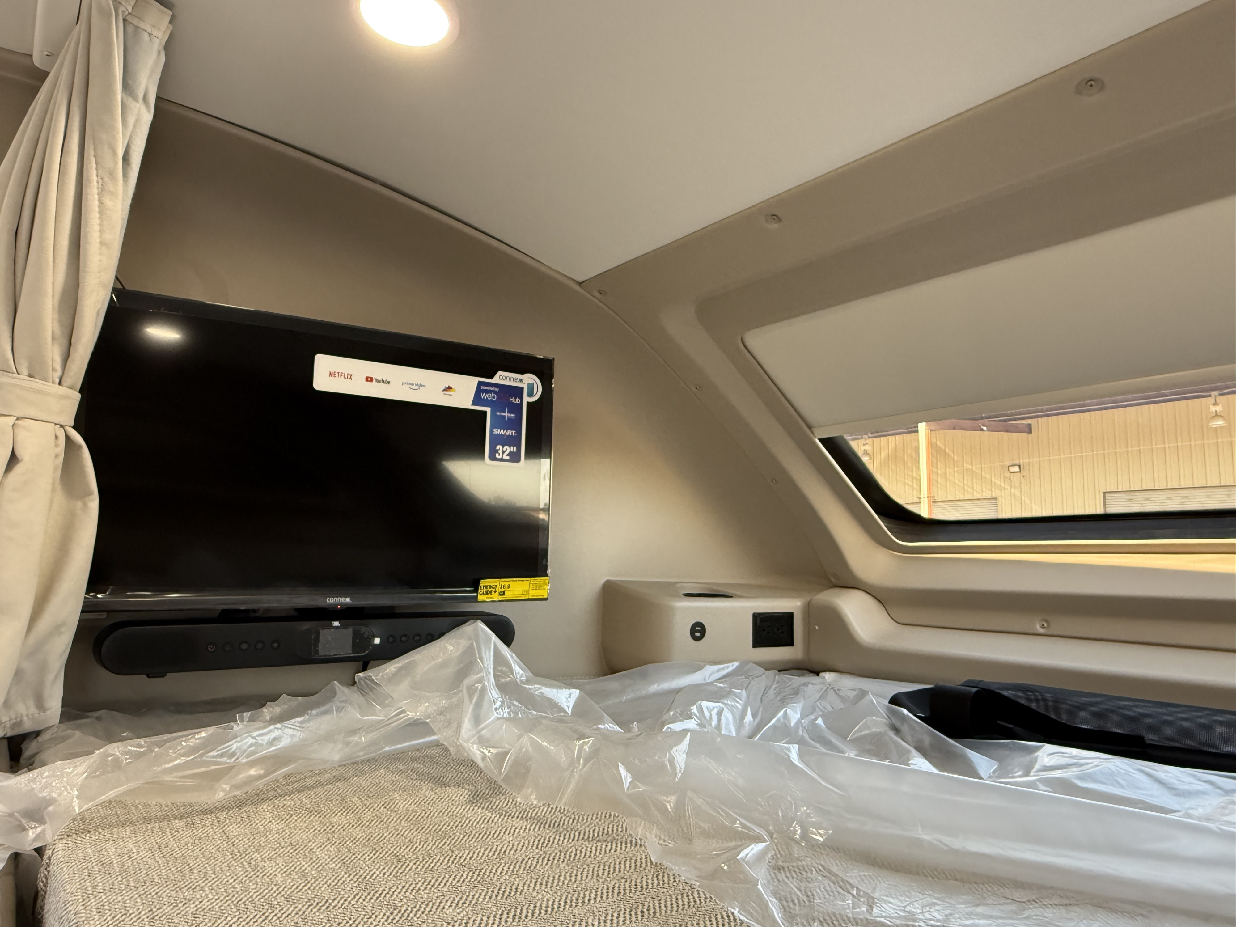 RV rental interior: A protected bed, 32" smart TV & soundbar, and power outlets by a window, ready for travel.. Entegra Coach Esteem 2025