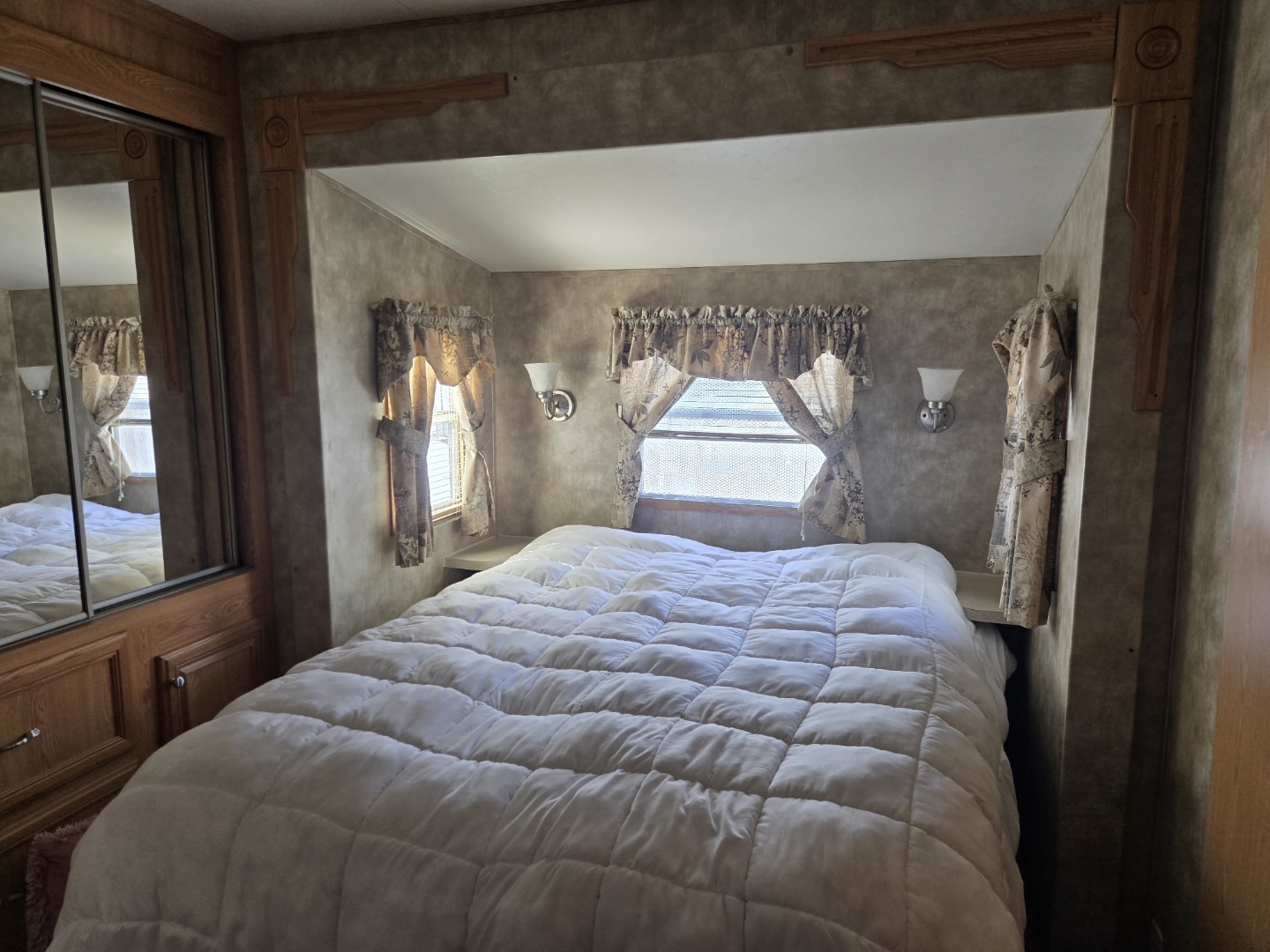 RV rental bedroom: A cozy interior with a large bed, patterned window curtains, and a mirrored wardrobe on the left.. Breckenridge Other 2008