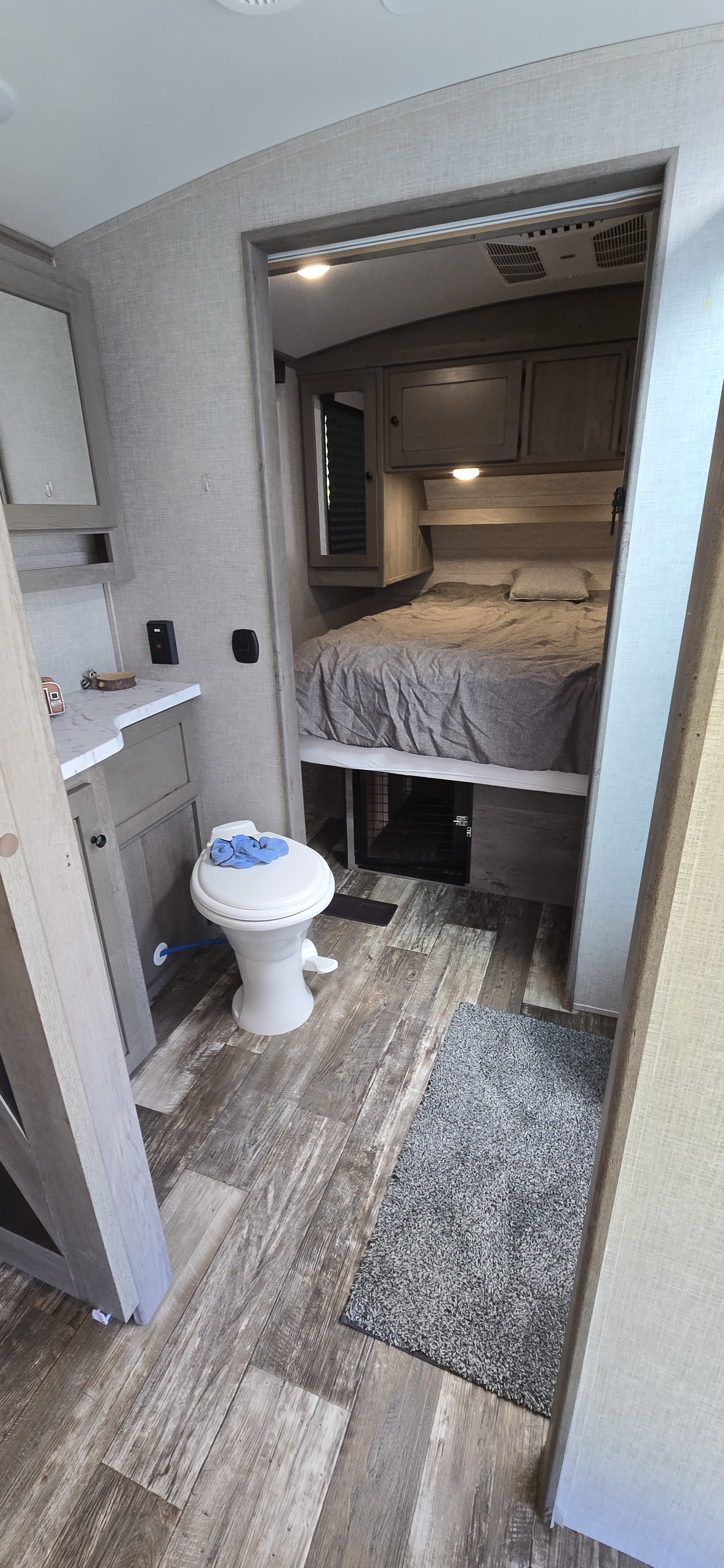 Cozy RV rental with compact toilet & vanity, leading to a bedroom featuring a bed over a pet crate.. Keystone RV Outback Ultra-Lite 2020